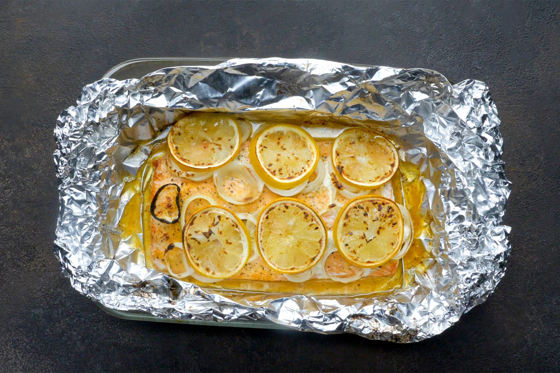 Overhead shot of unfold foil; baked salmon in a large baking pan; dark grey background;