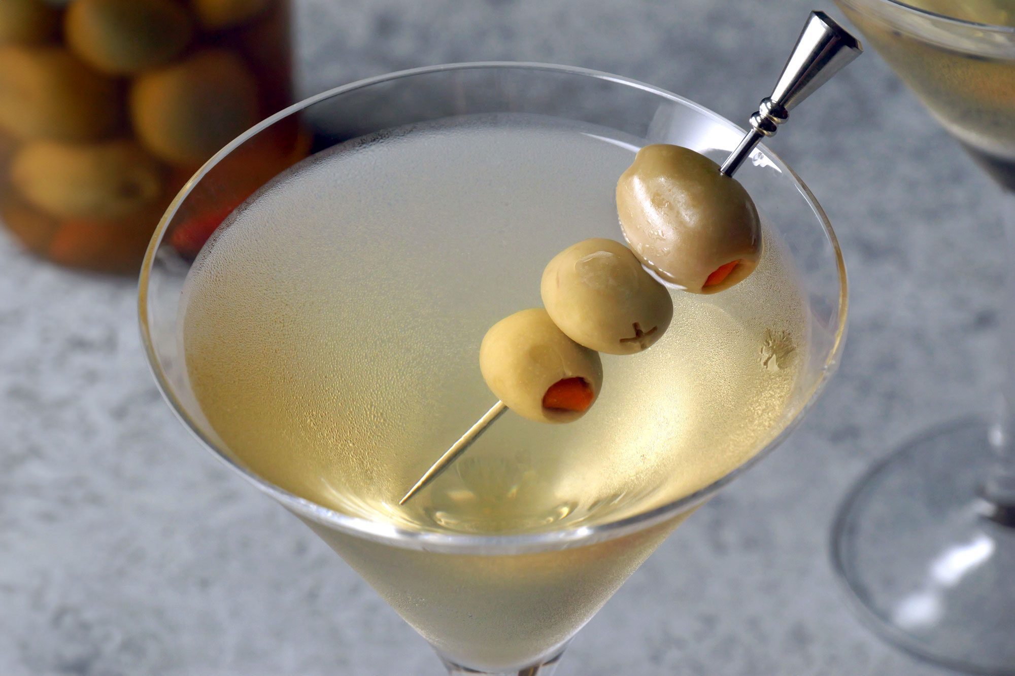 3/4 angle view shot of Dirty Martini; into martini glass; garnish with oilves; grey background;