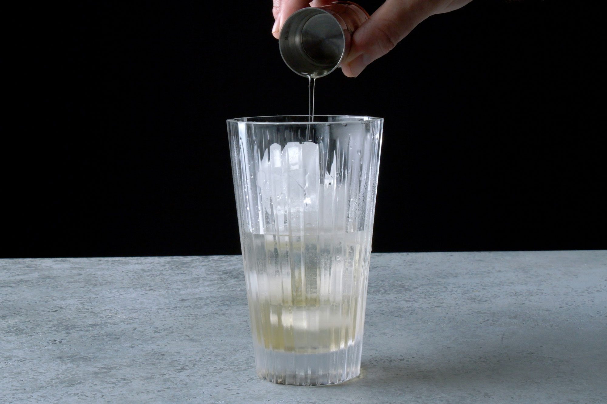 Table view shot of combine vodka; vermouth and oilve brine in a mixing glass with ice; grey background;