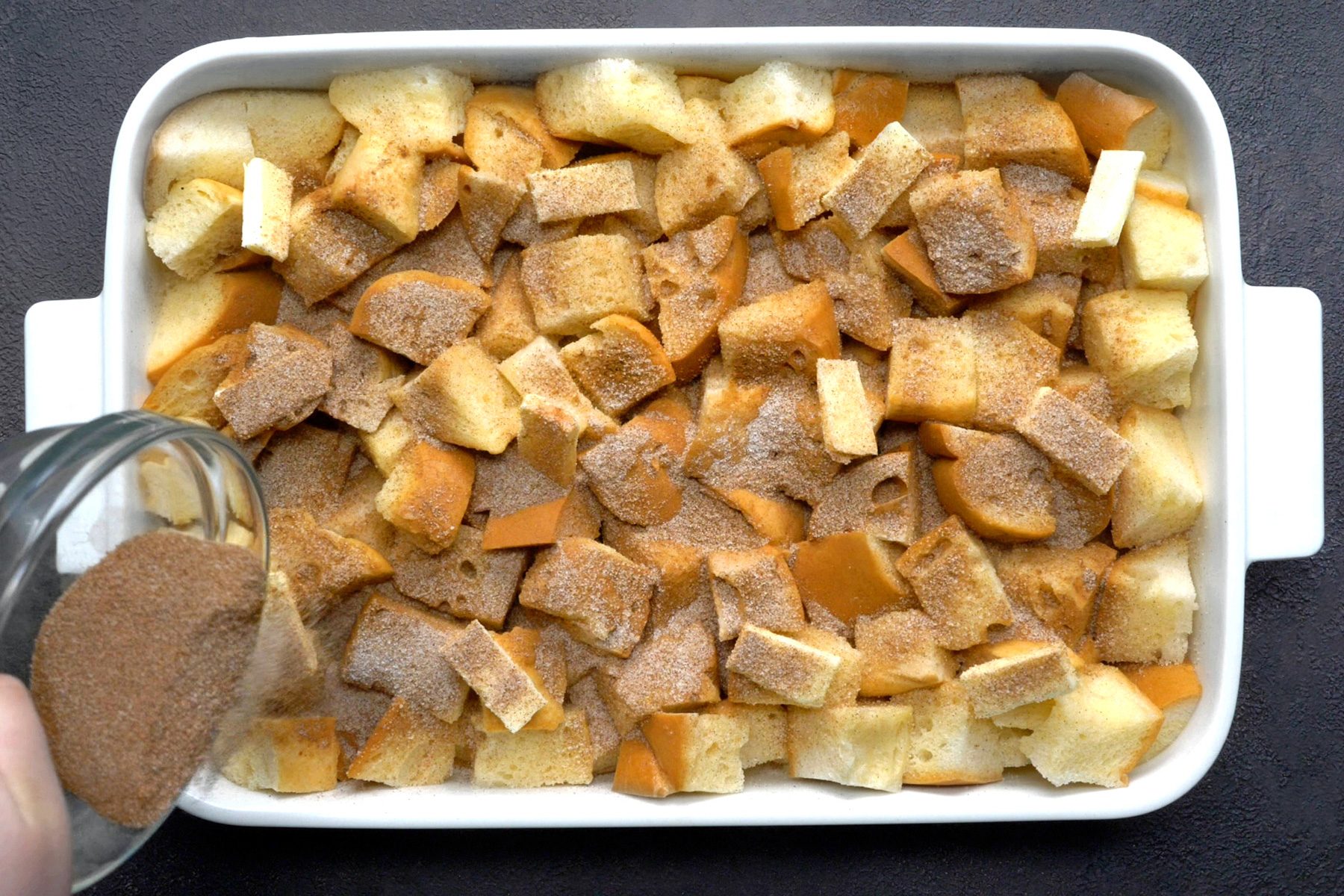 A baking dish filled with French bread cubes topped with the mixture of sugar and cinnamon.