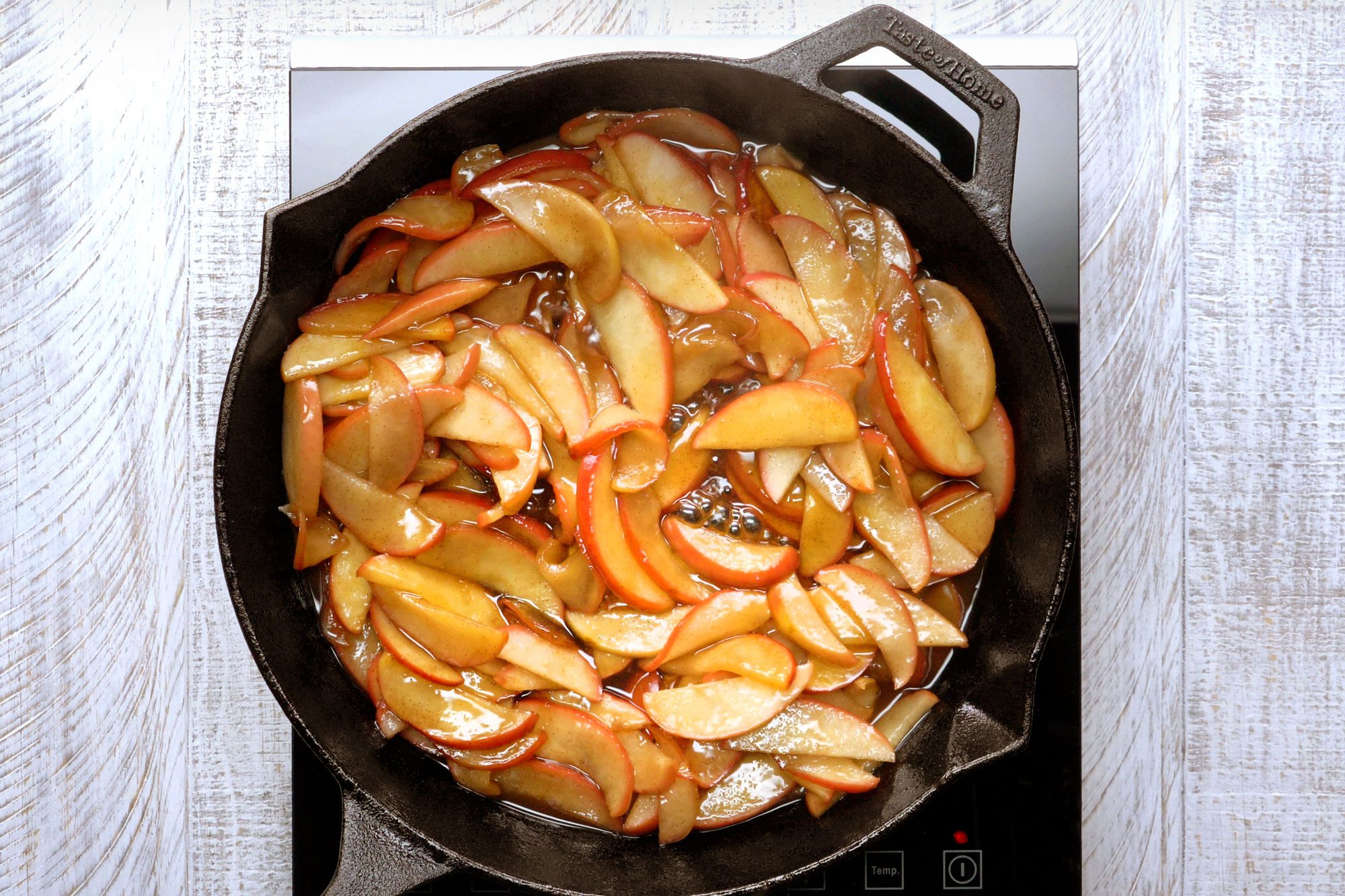 Overhead shot of fried apples in a large cast-iron skillet on wooden background