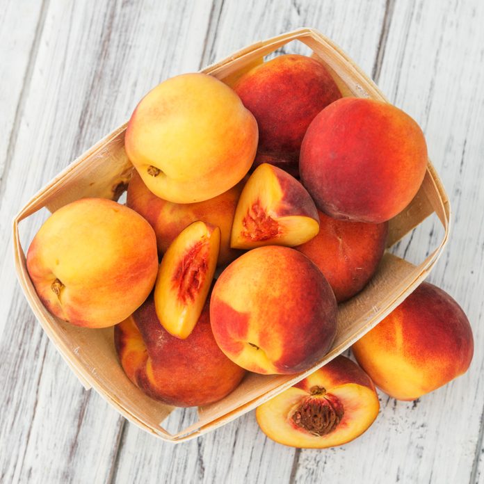 peaches in a wooden container on white wood surface