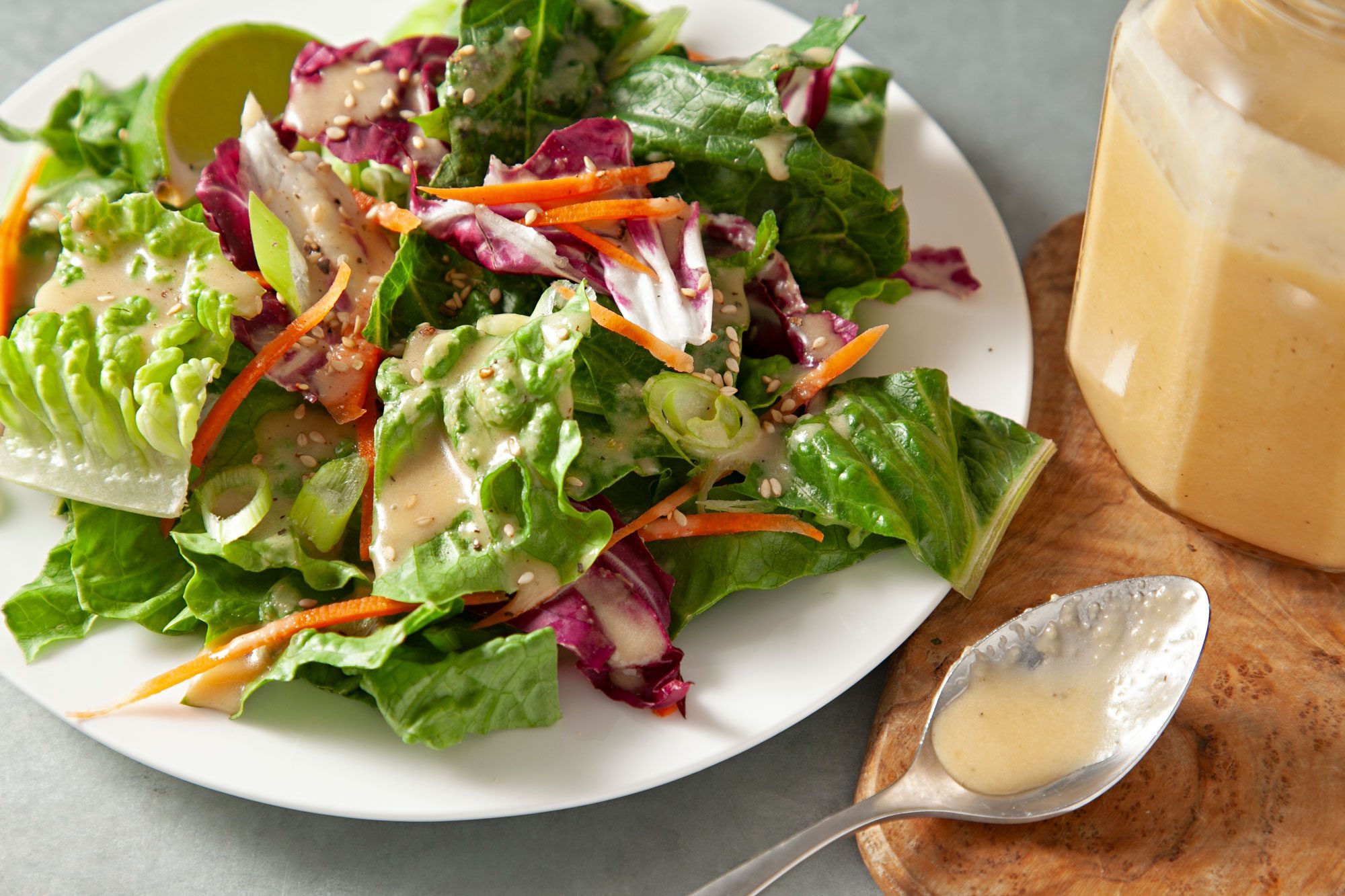 Ginger Dressing spread over salad in small white plate; ginger dressing in a glass jar placed over wooden board with small spoon