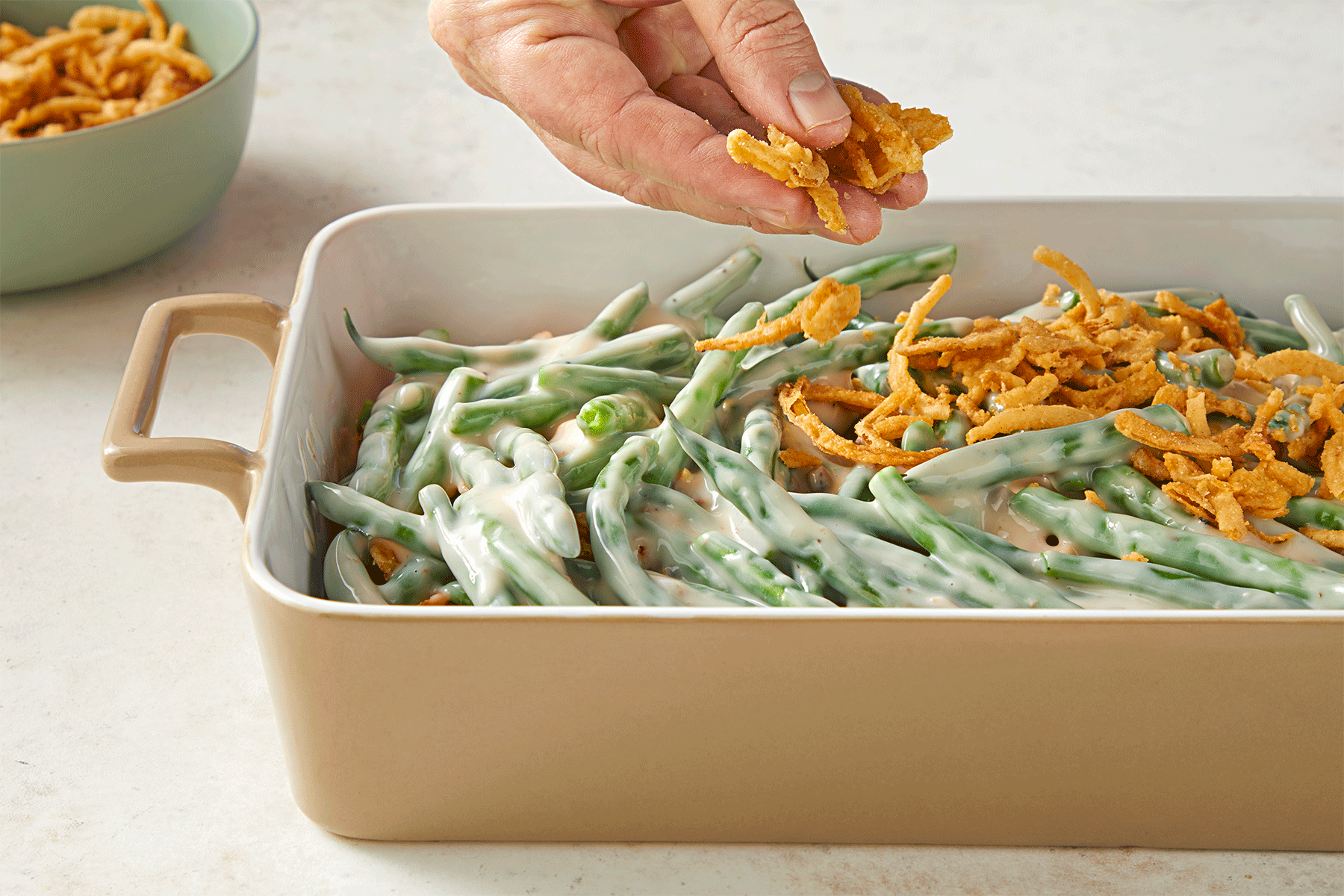 A close-up of a rectangular baking dish filled with green bean casserole topped with crispy fried onions.