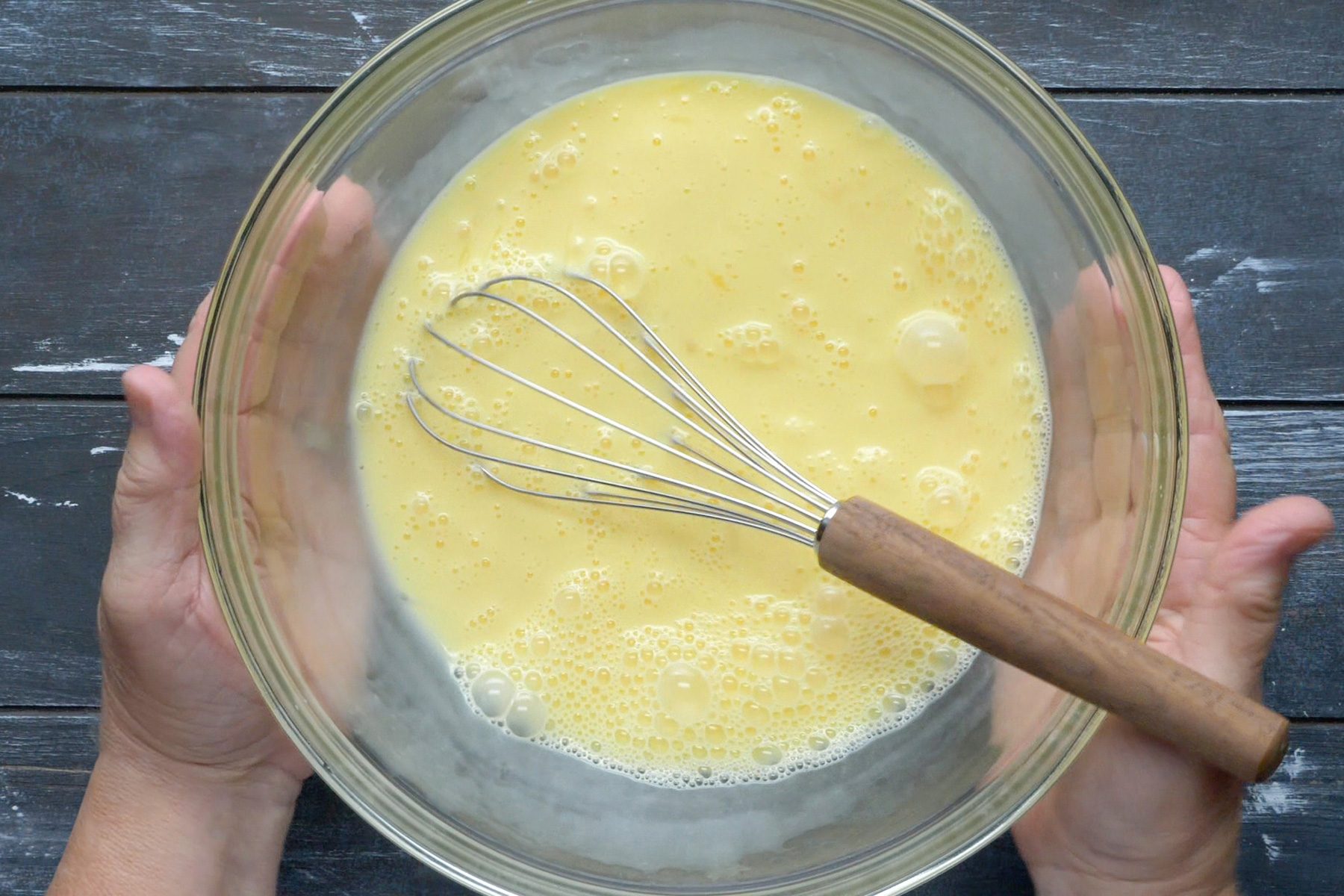 A bowl with a mixture of eggs and milk, along with a whisk