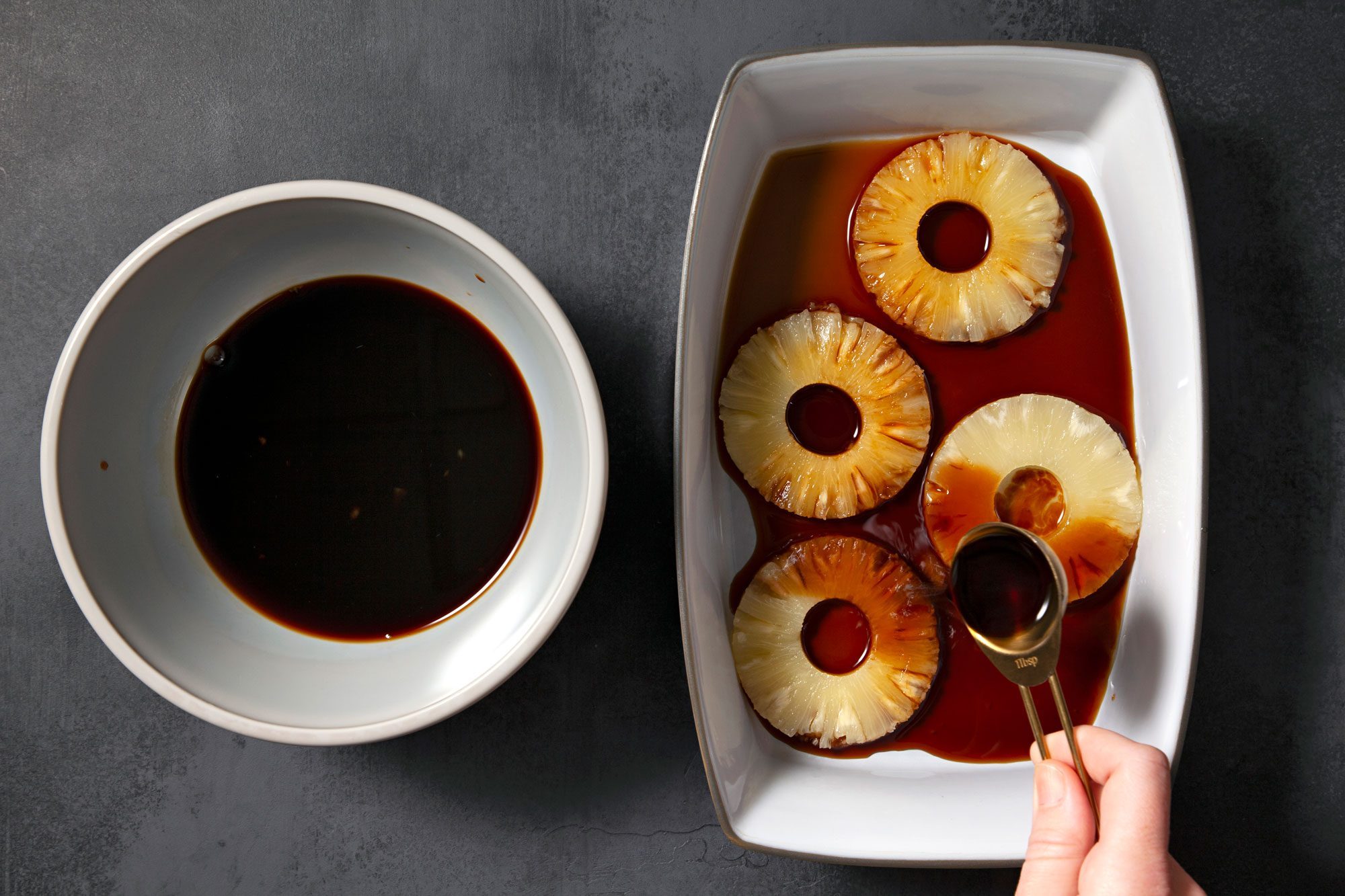 overhead shot; black background; in a shallow dish add pineapple slices; pineapple juice into a small bowl with teriyaki sauce;