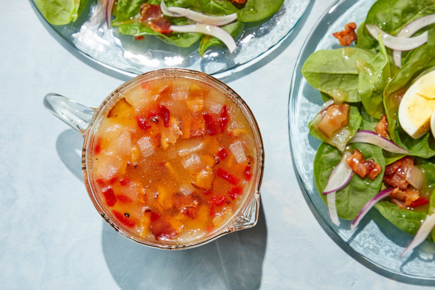 Top view shot of Hot Bacon Dressing; in a cup; pour over salad; served on plates; light blue background