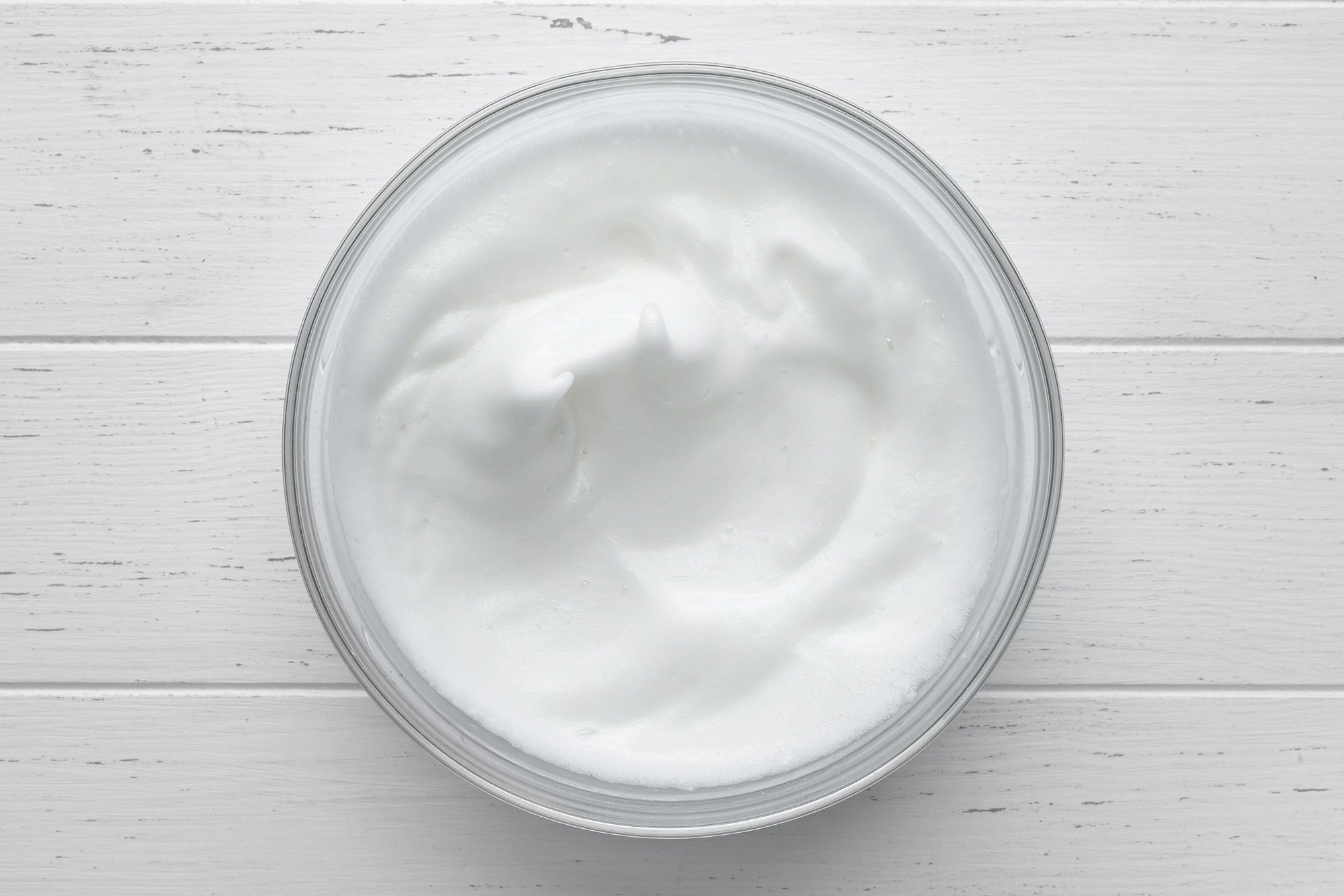 Overhead shot of beated egg whites in a large bowl; white wooden background;