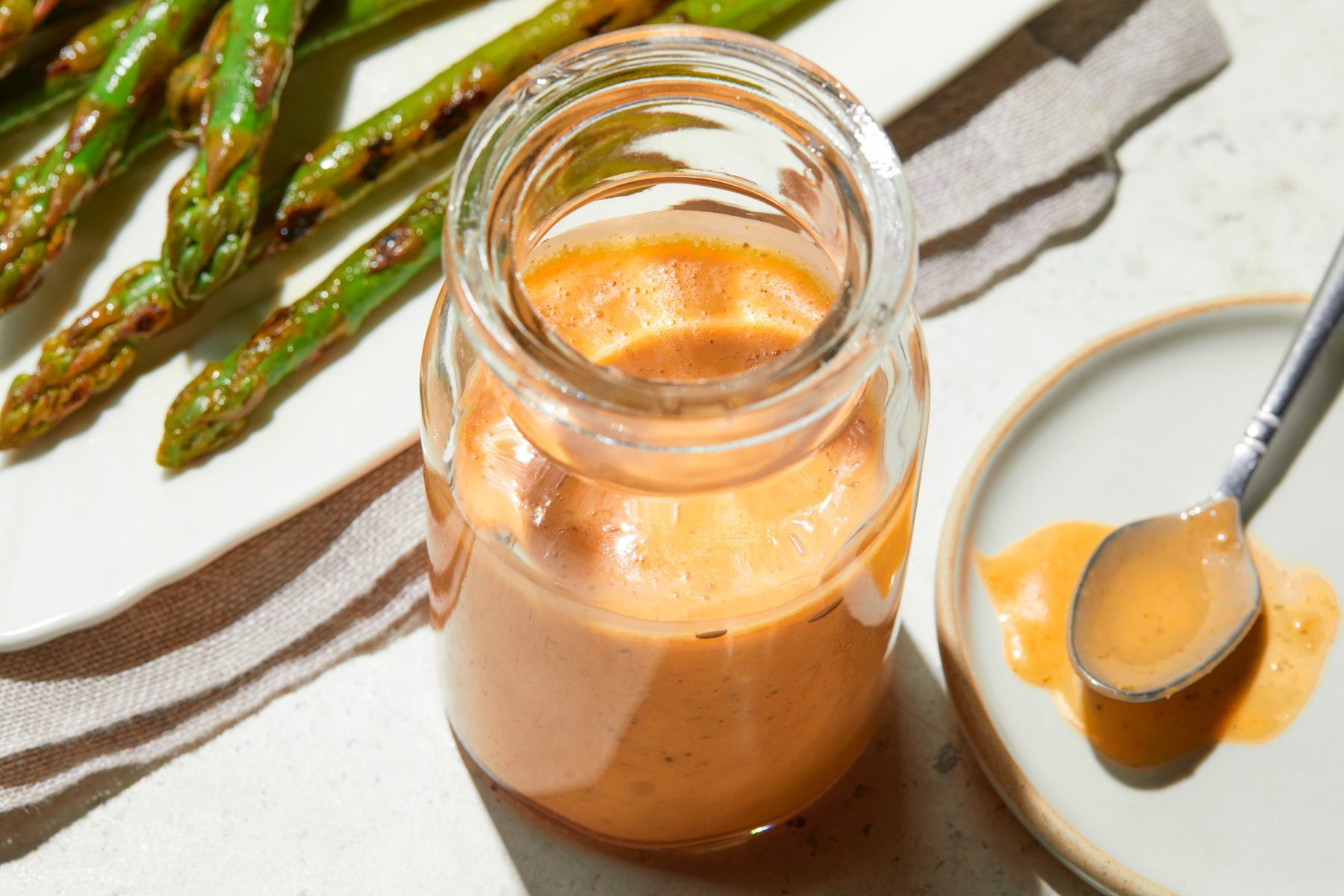 A Jat of Italian Dressing next to a plate of asparagus on a table