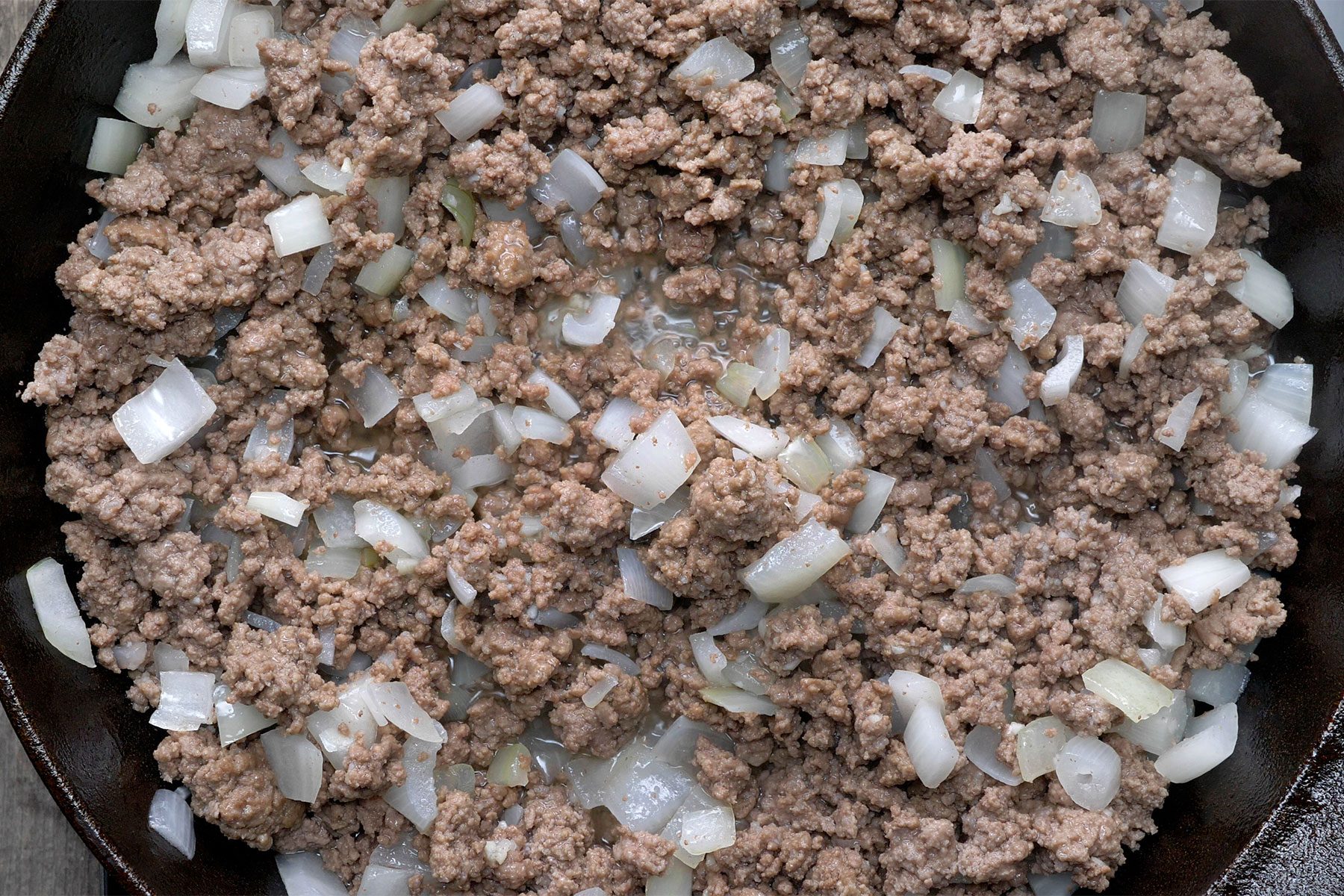 Overhead shot of cooked beef and onion over medium heat until no longer pink in a large skillet; wooden background;