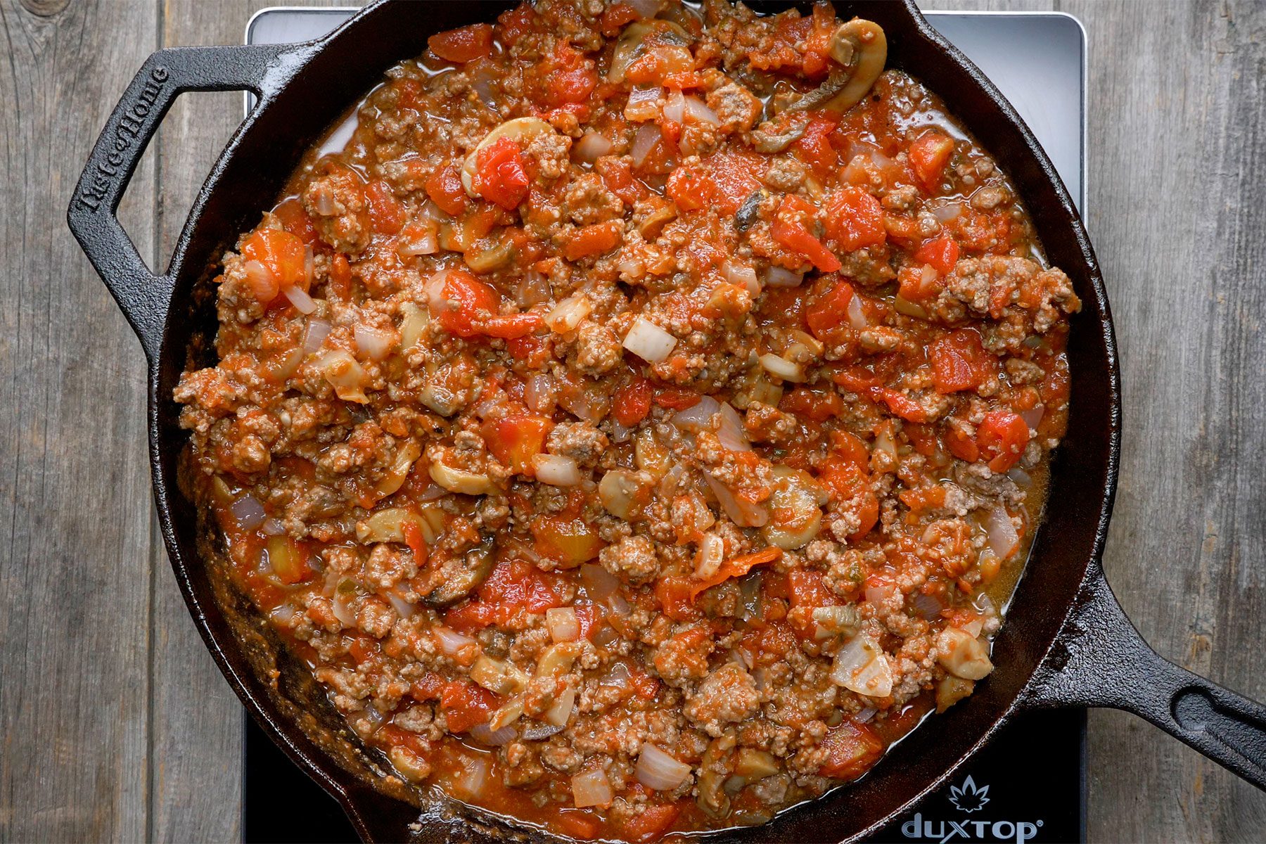 Overhead shot of stir in spaghetti sauce; diced tomatoes; mushrooms and italian seasoning; induction stove;wooden background;