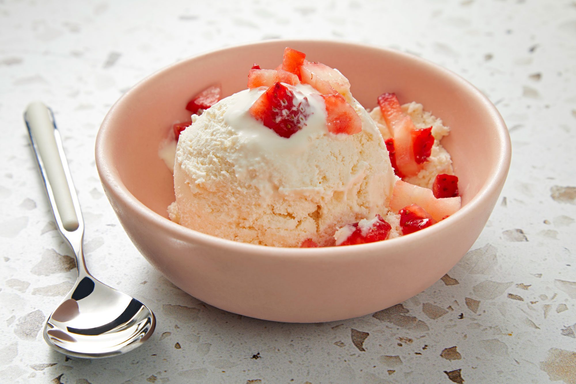 A bowl of Keto Ice Cream topped with strawberries, served with a spoon