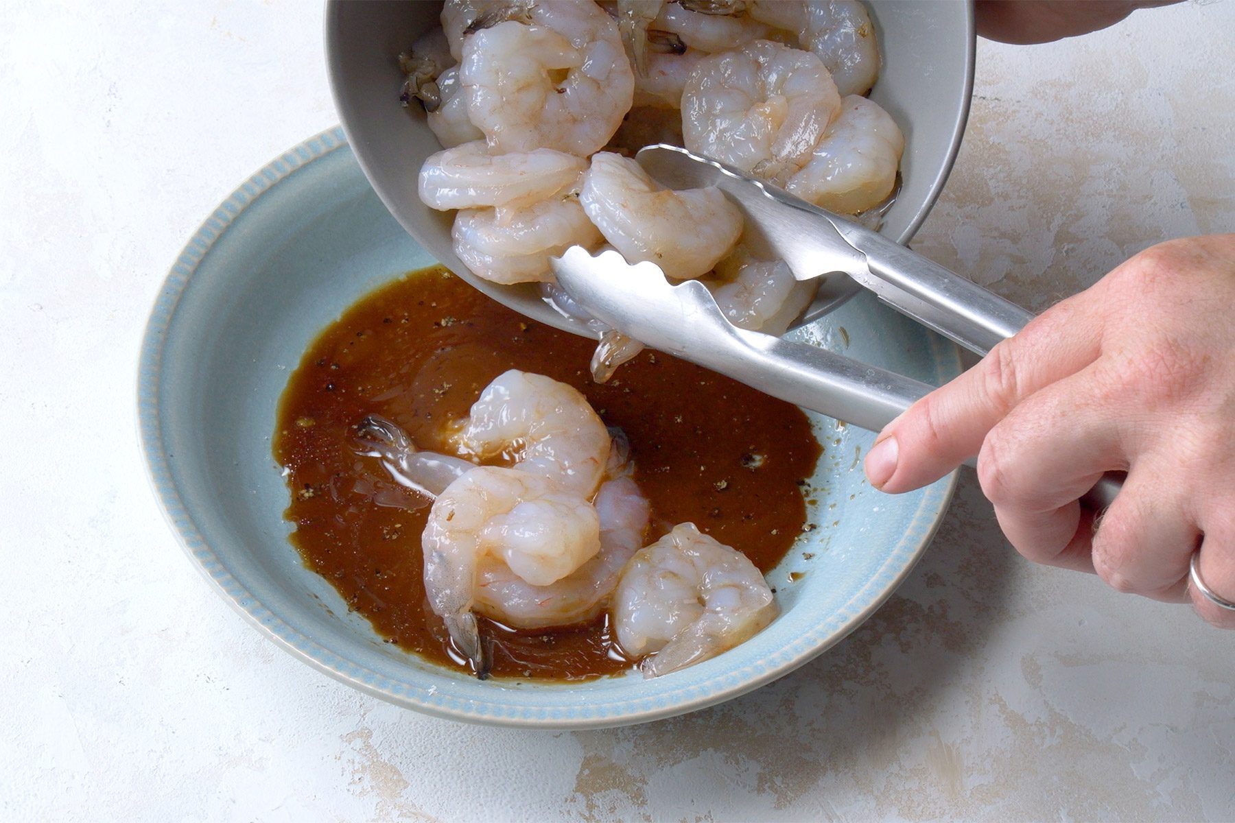 High angle view shot of whisk Shaoxing wine; soy sauce; cornstarch; oil; oyster sauce; sugar and pepper in a large bowl; stir in shrimp; tongs; marble background