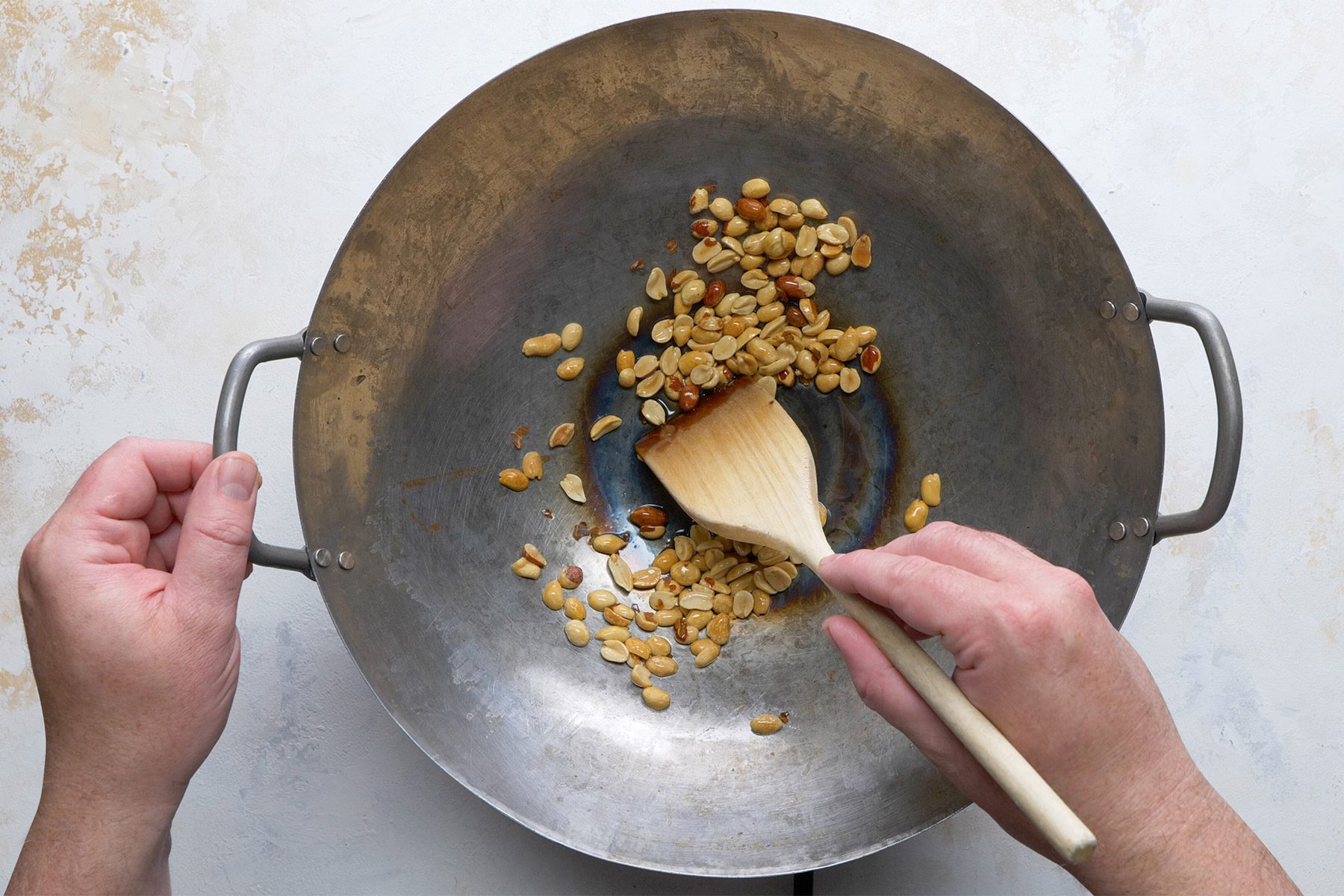 Overhead shot of a large skillet; heat 1 tablespoon oil over medium-high heat; add peanuts; cook and stir until lightly browned; slotted spoon; remove peanuts; marble background