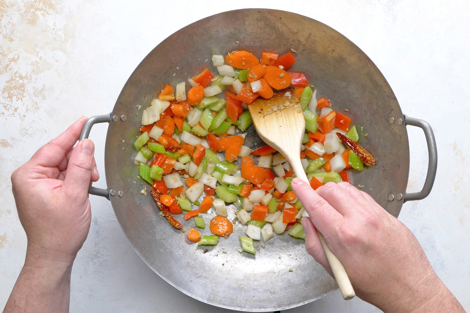 Overhead shot of a same skillet; heat remaining 1 tablespoon oil over low heat; add chiles; cook and stir; add garlic and ginger; again cook and stir; add carrots and celery again cook and stir; add onion and sweet red pepper; cook and stir until vegetables are crisp-tender; marble background