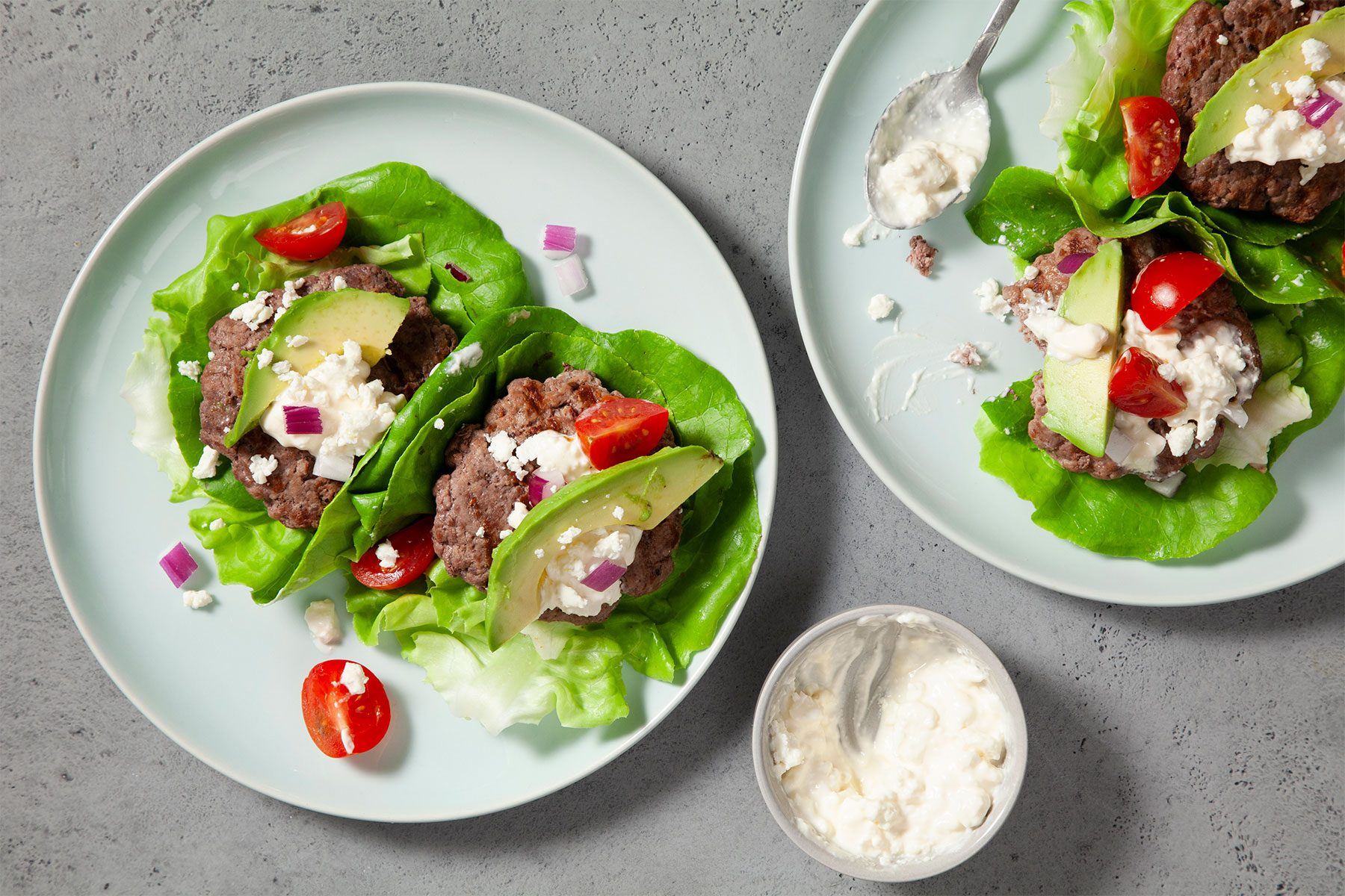 Overhead shot of Calofornia Burger Wraps; served on two white plates; with feta and miracle whip; grey marble background;