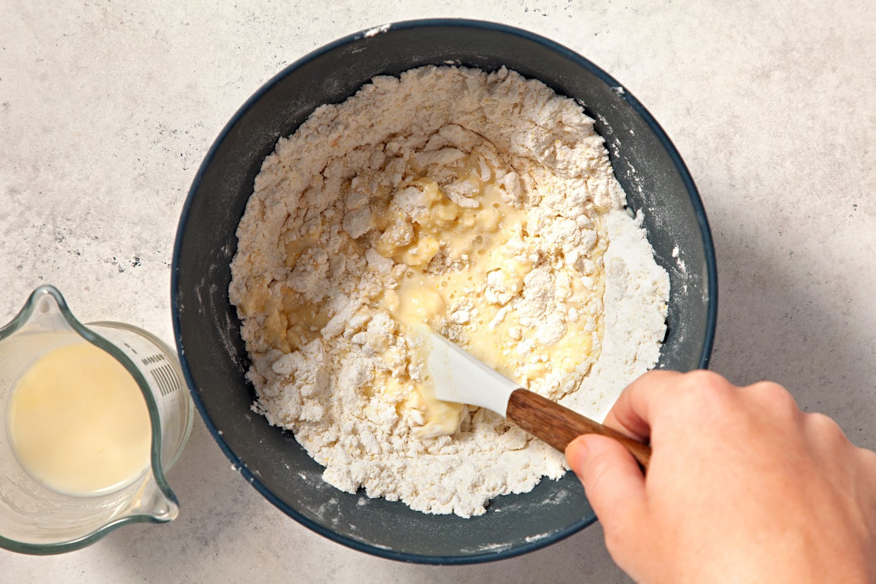 A hand is mixing flour with milk, egg, and other ingredients in a bowl