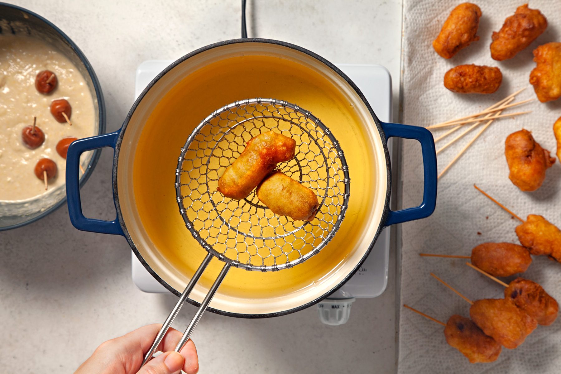 A hand is frying battered mini corn dogs in oil