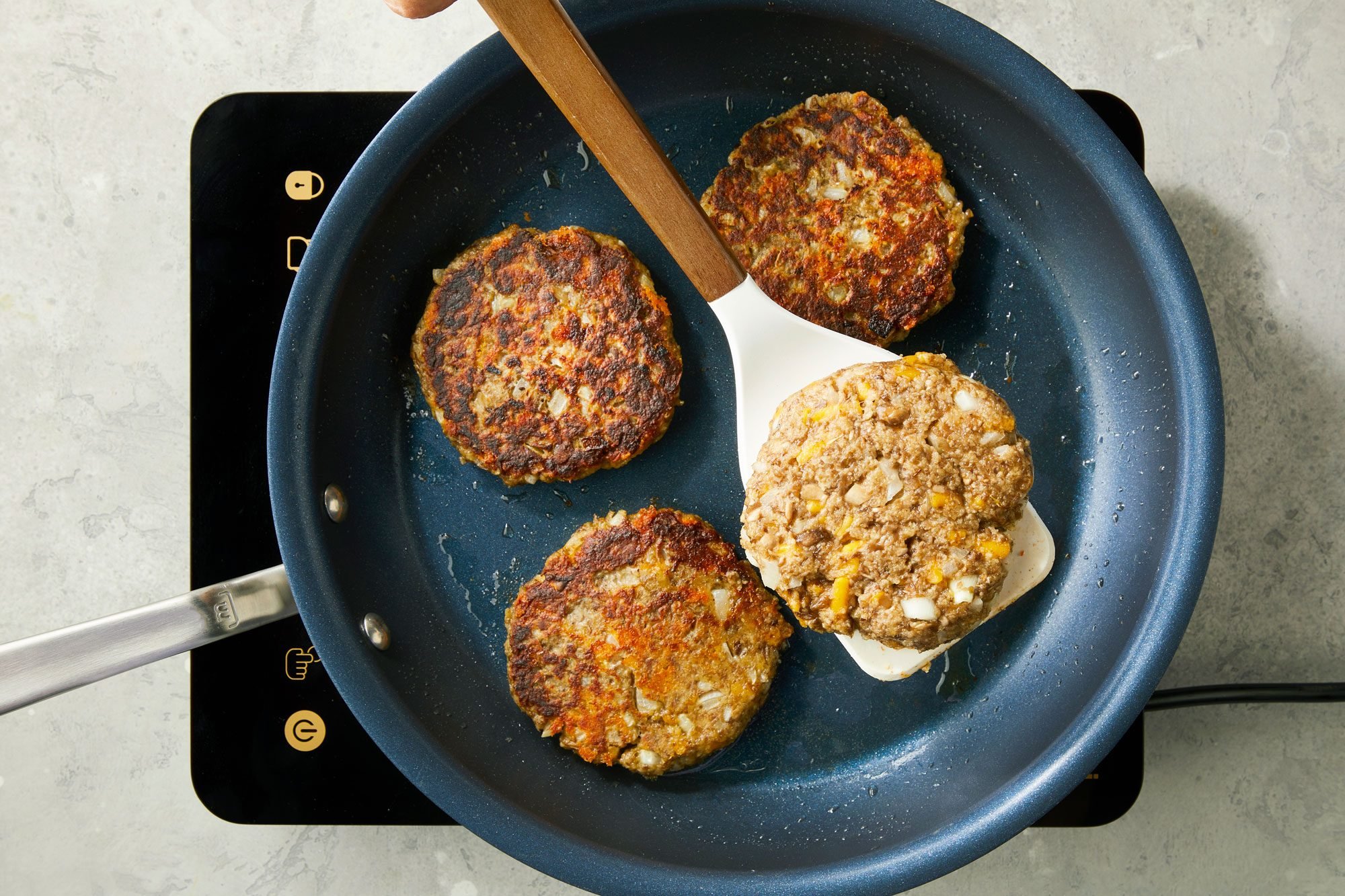 overhead shot; grey background; Frying and flipping patties, In a large cast-iron skillet;
