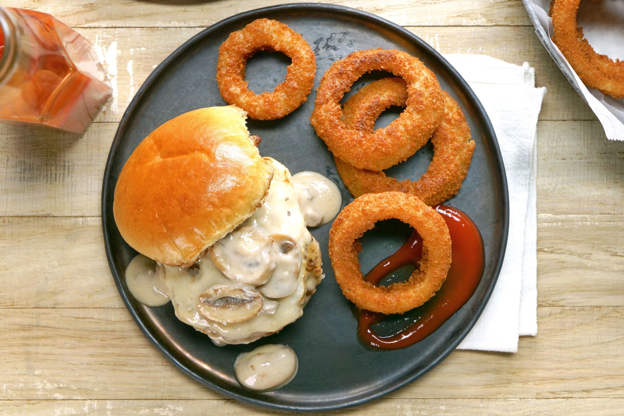 A plate with a Mushroom Swiss Burger and onion rings on the side