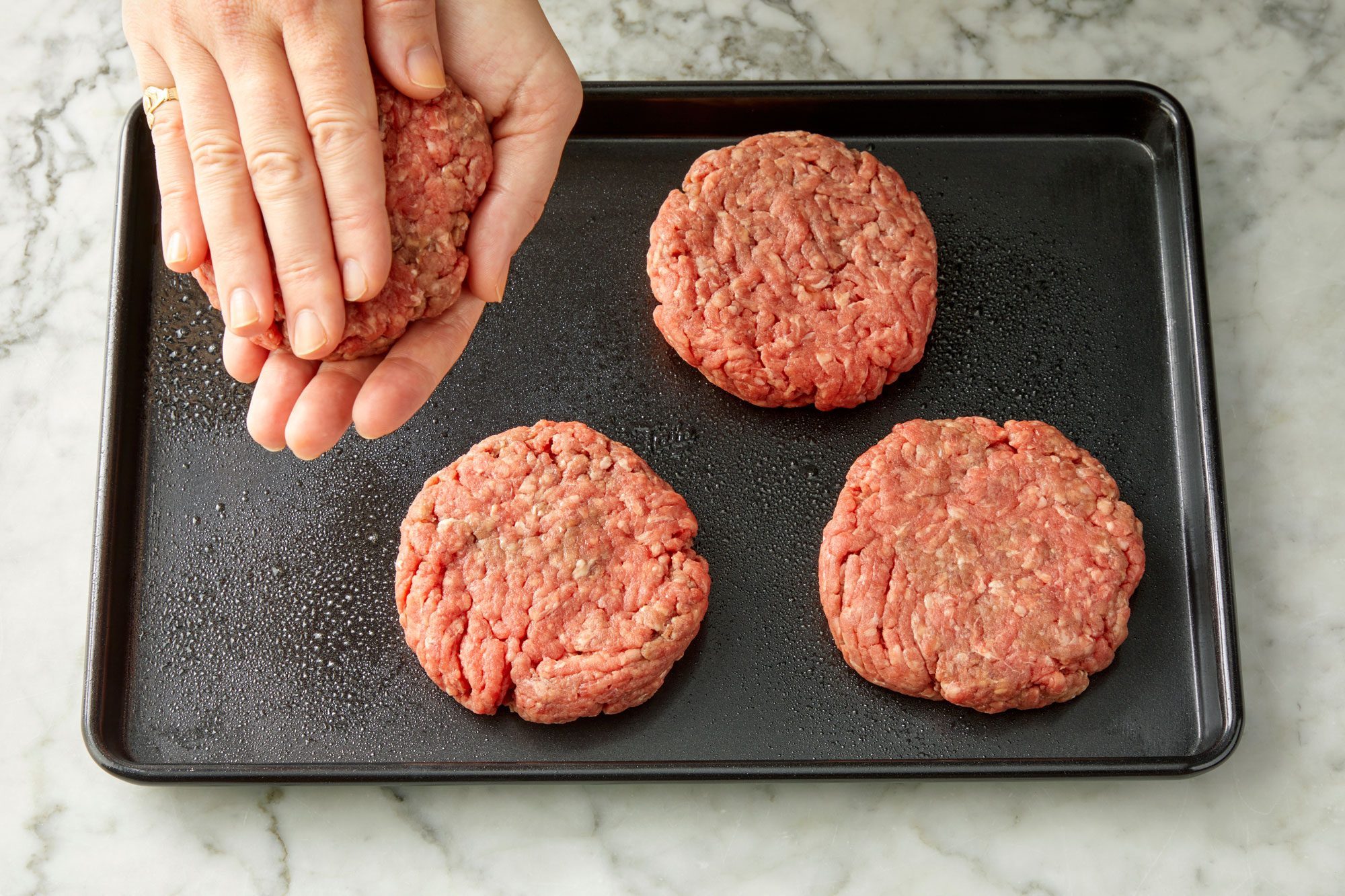 Top view shot of shape ground beef into four thick patties; marble background;