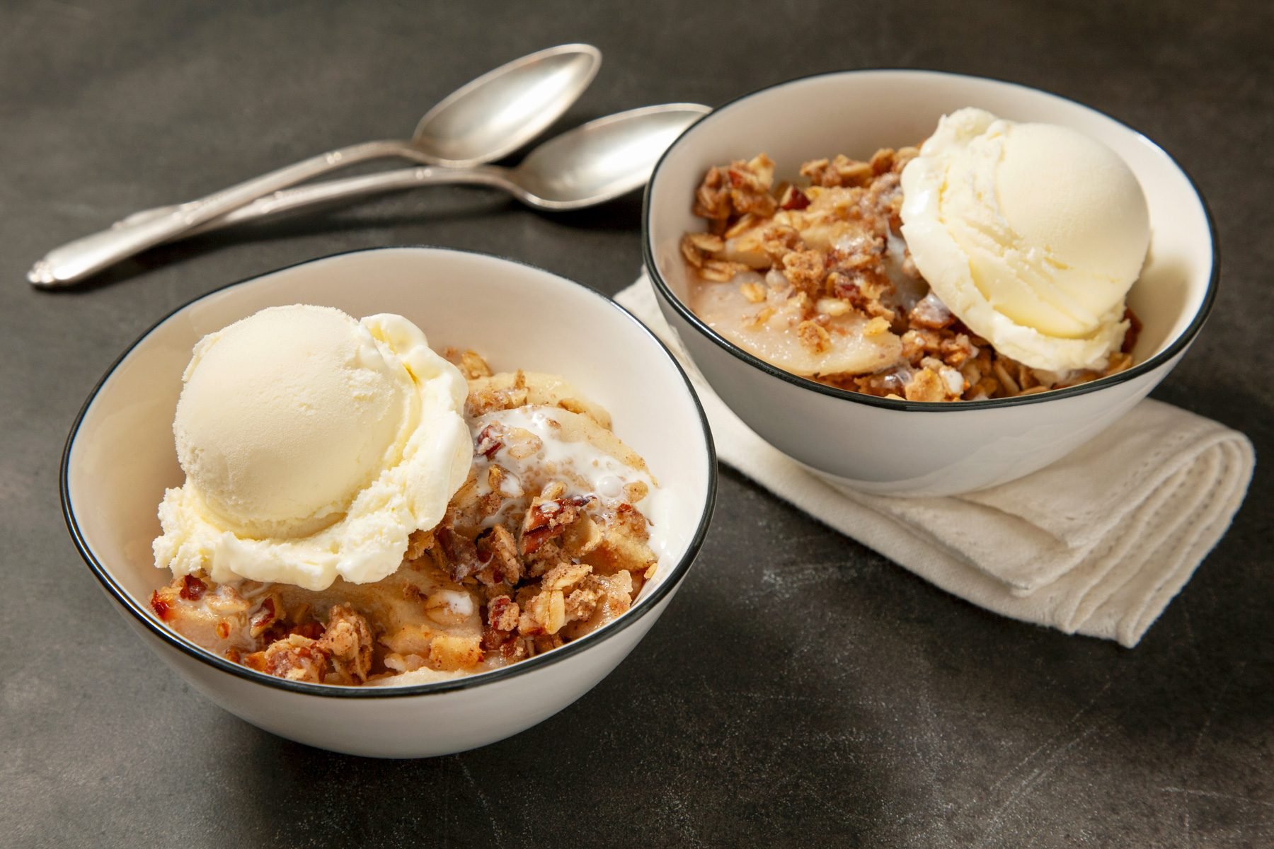 Two bowls of pear crumble served with a scoop of vanilla custard ice cream