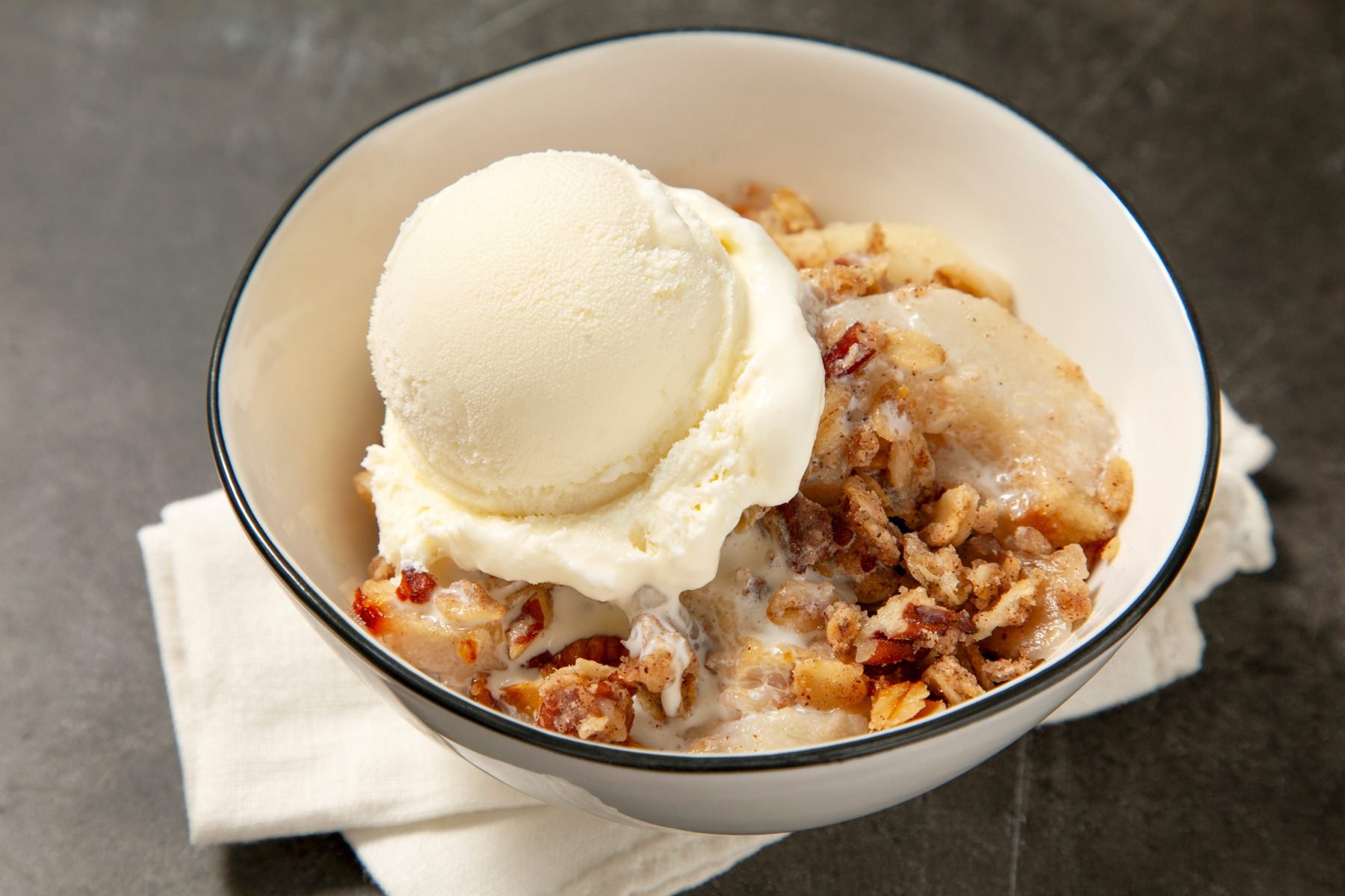 A bowl of pear crumble served with a scoop of vanilla custard ice cream