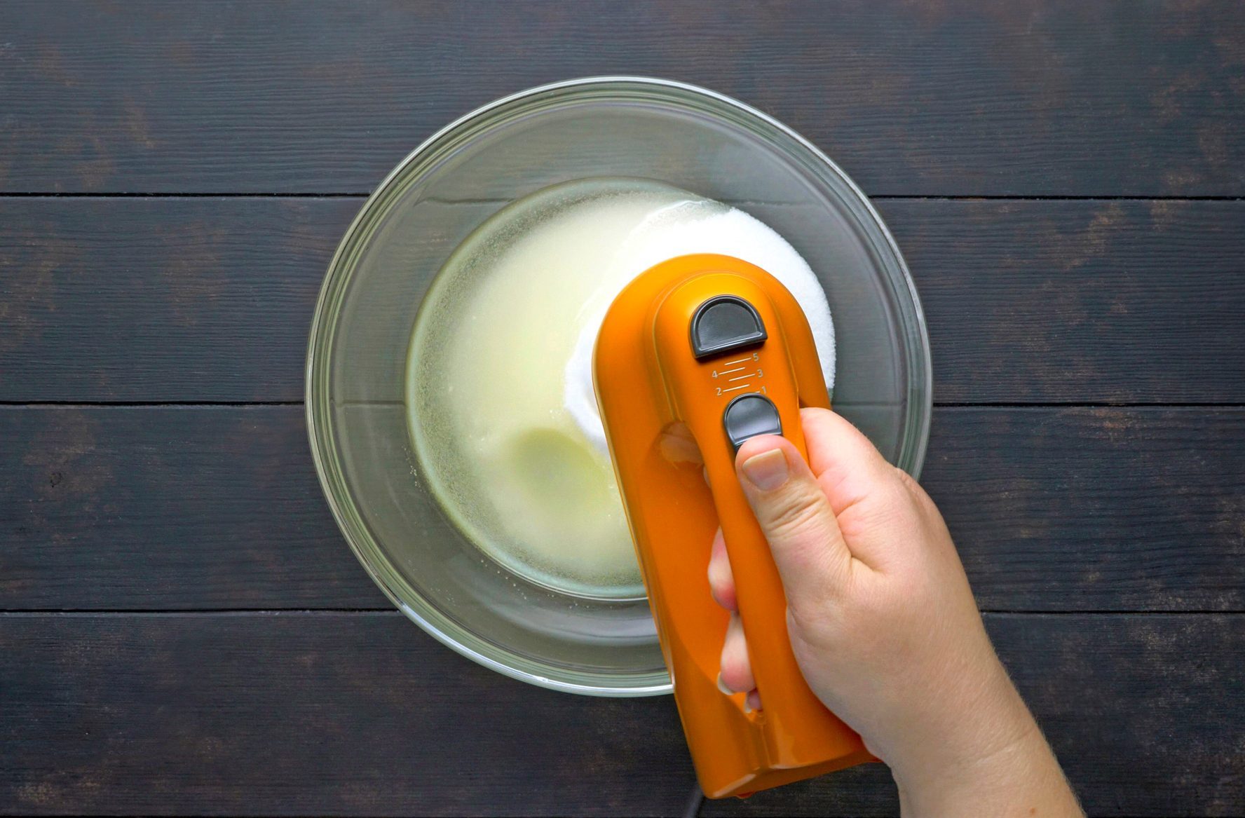 A Hand mixing the oil and sugar in a glass bowl