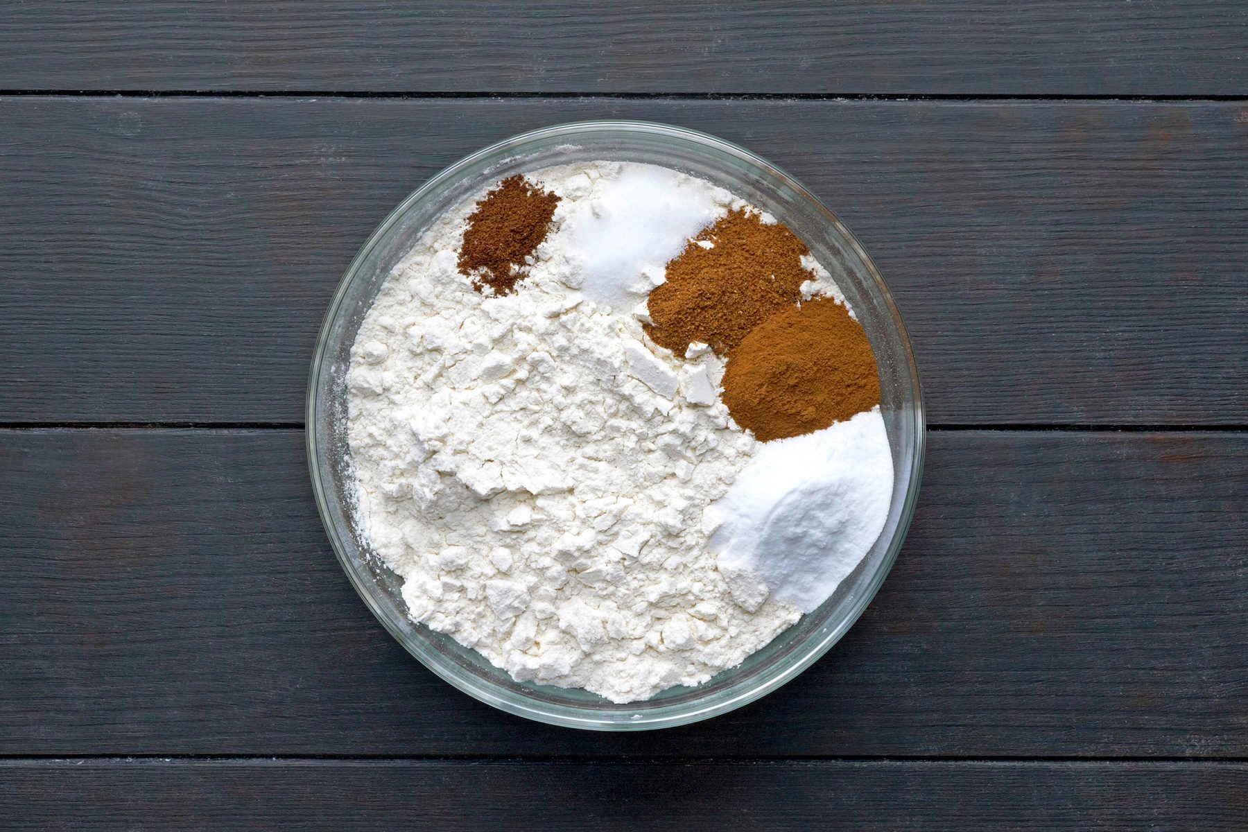 A bowl with flour, baking soda, cinnamon, nutmeg, salt and ground cloves on a table