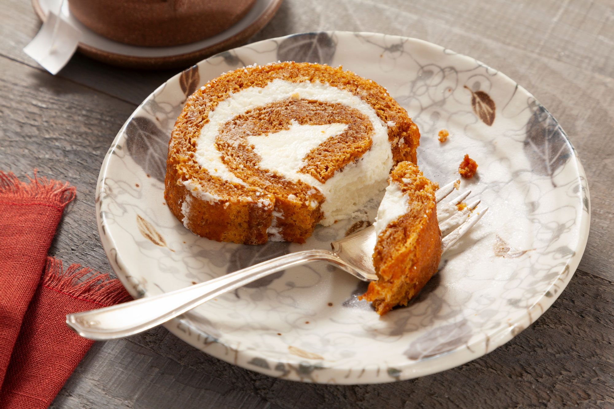 3/4 angle shot of Pumpkin Roll served on small fancy plate with fork; wooden background;