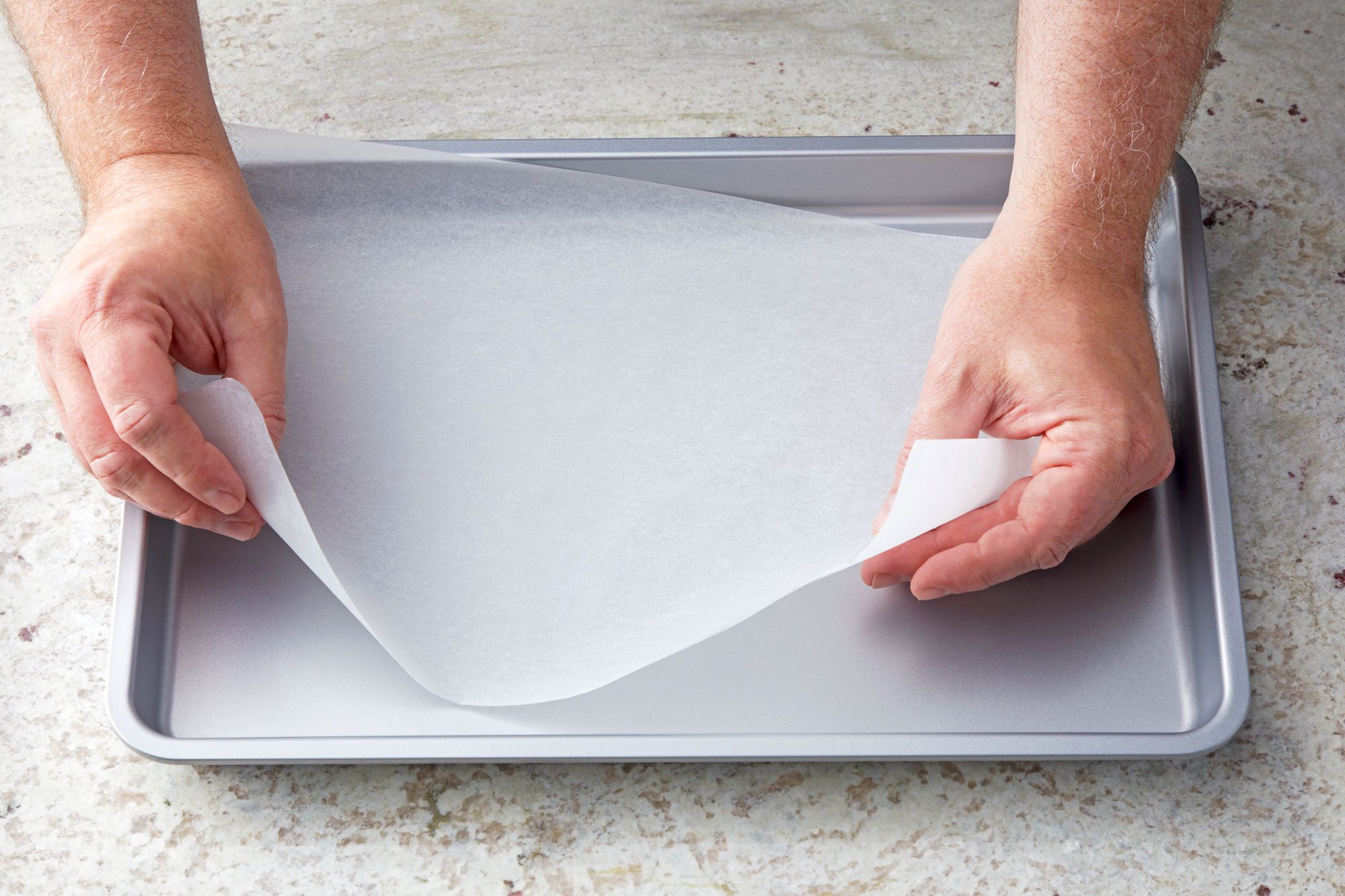 3/4th shot; white textured background; placing waxed paper over baking pan;