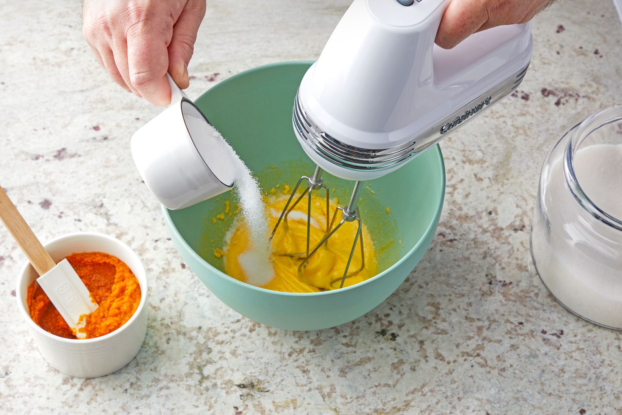 3/4th shot; white textured background; In a large bowl, beating egg yolks with electric whisker, Gradually adding sugar;