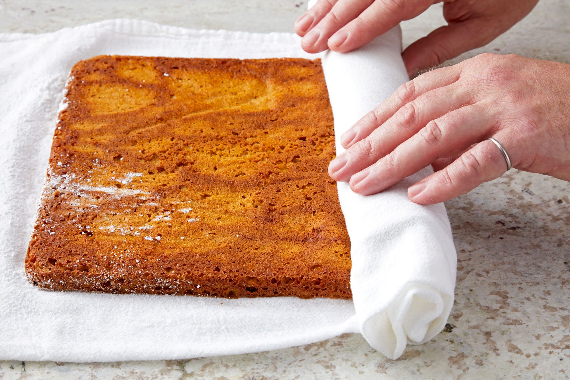 horizontal shot; Rolling up cake in the towel jelly-roll style, starting with a short side;