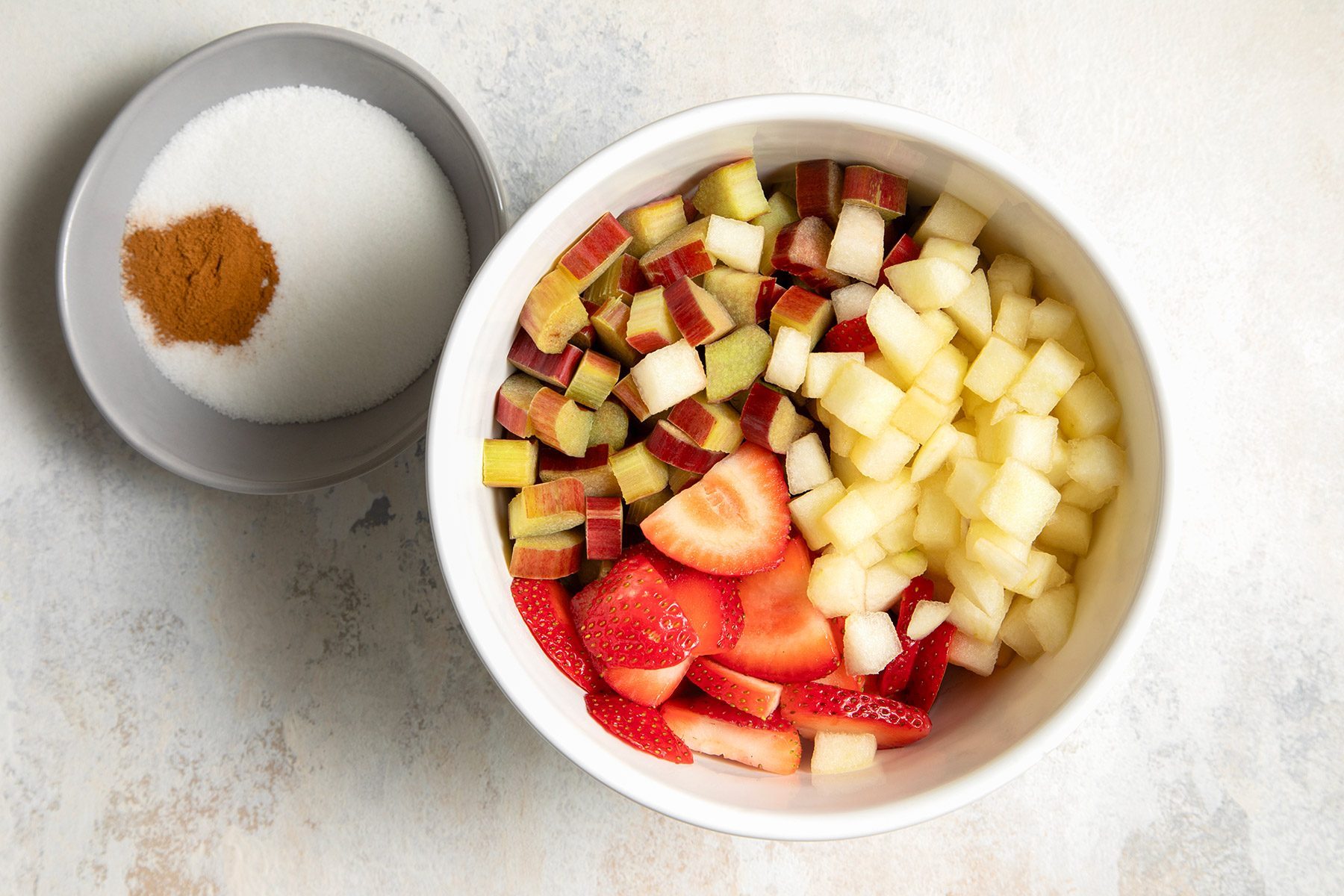 overhead shot of chopped fruits in a white bowl; sugar and cinnamon