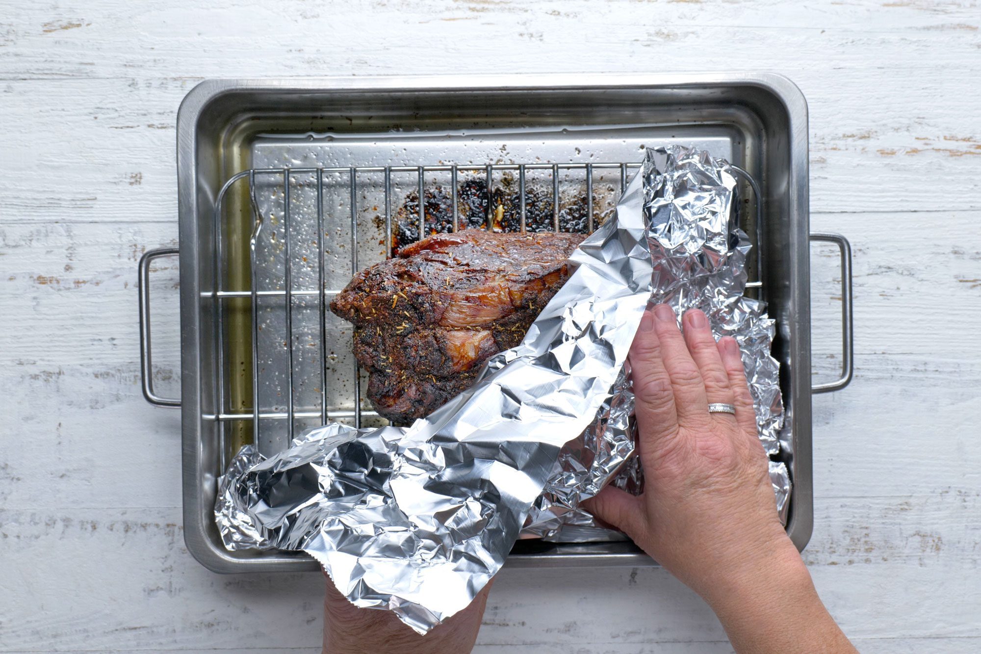 Overhead shot of roasting pan; roast until meat reaches desired doneness; remove from oven; tent with foil; white wooden background;