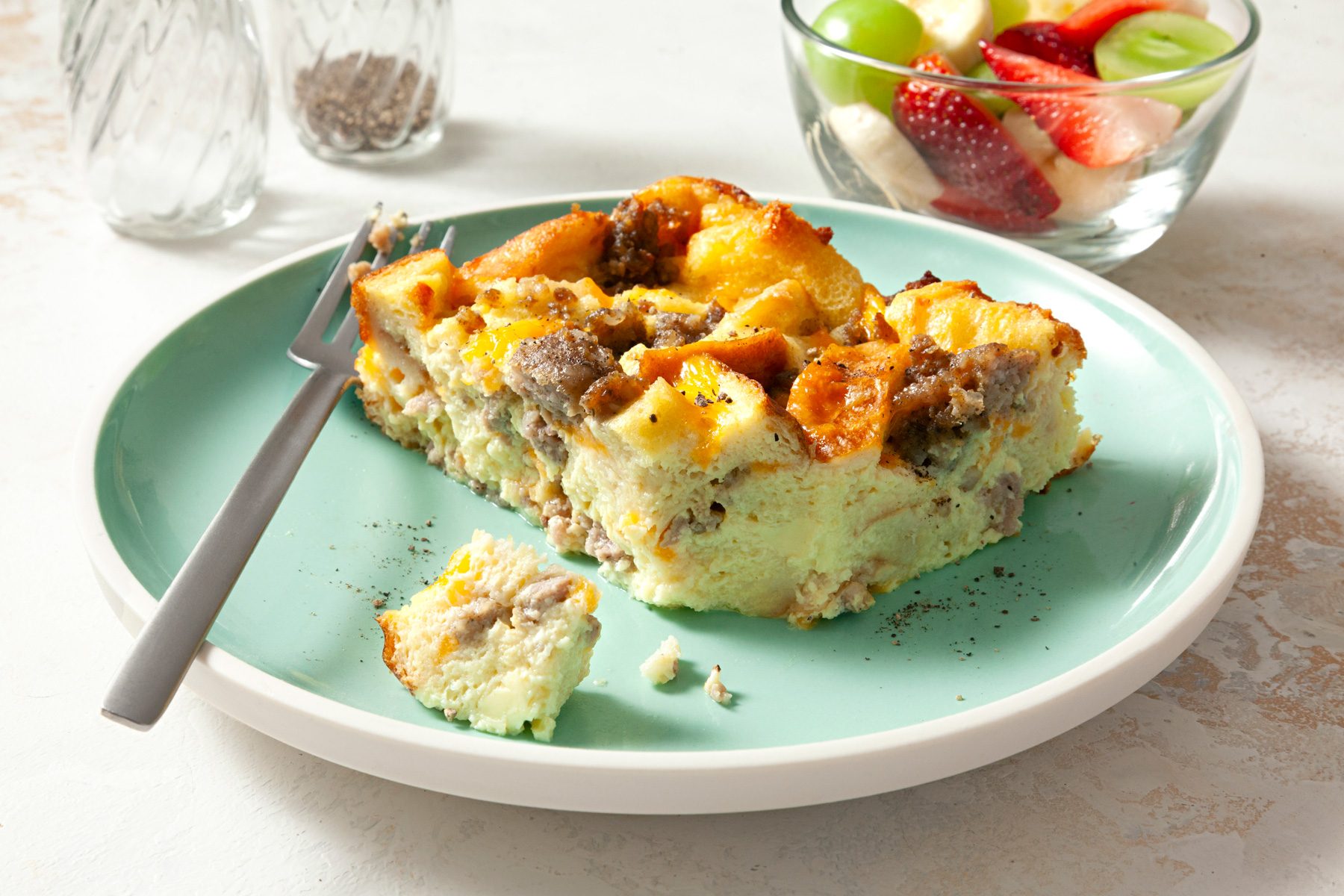 Sausage And Egg Casserole served on plate with a bowl of fresh fruits