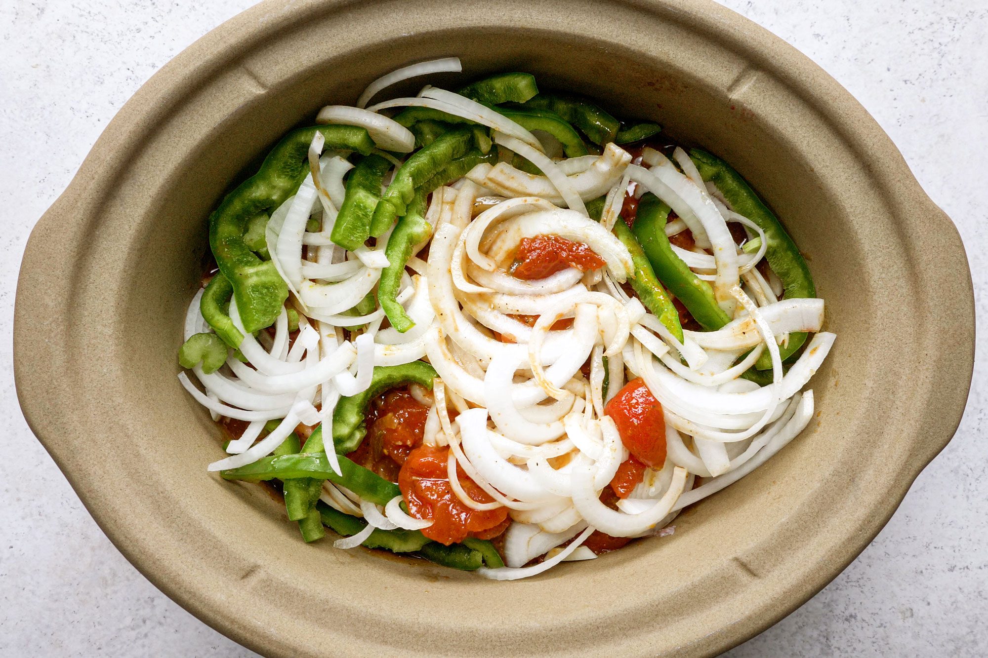 overhead shot of sliced vegetables in a slow cooker bowl