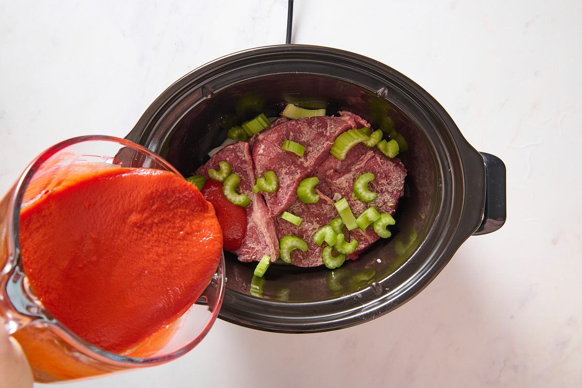 Pouring tomato sauce over steak in a slow cooker