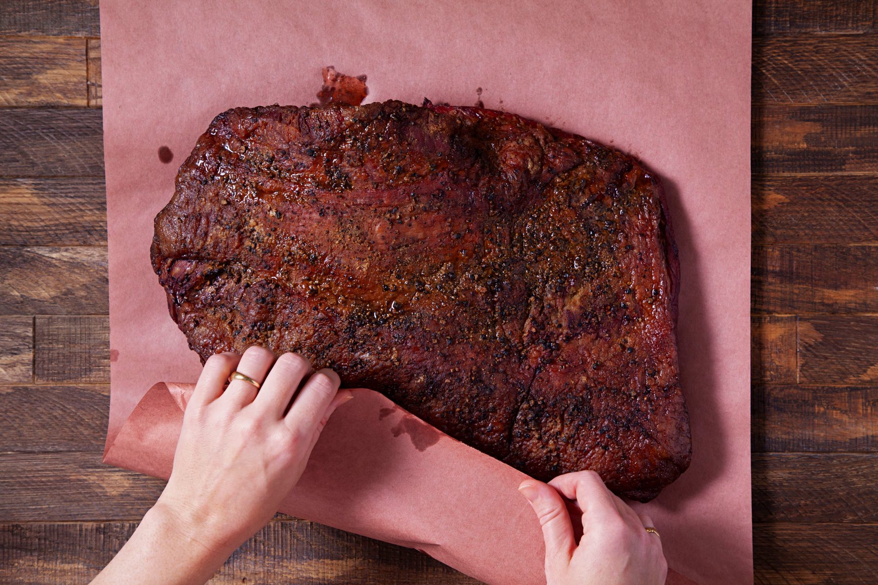 A person wrapping the brisket in unwaxed butcher paper
