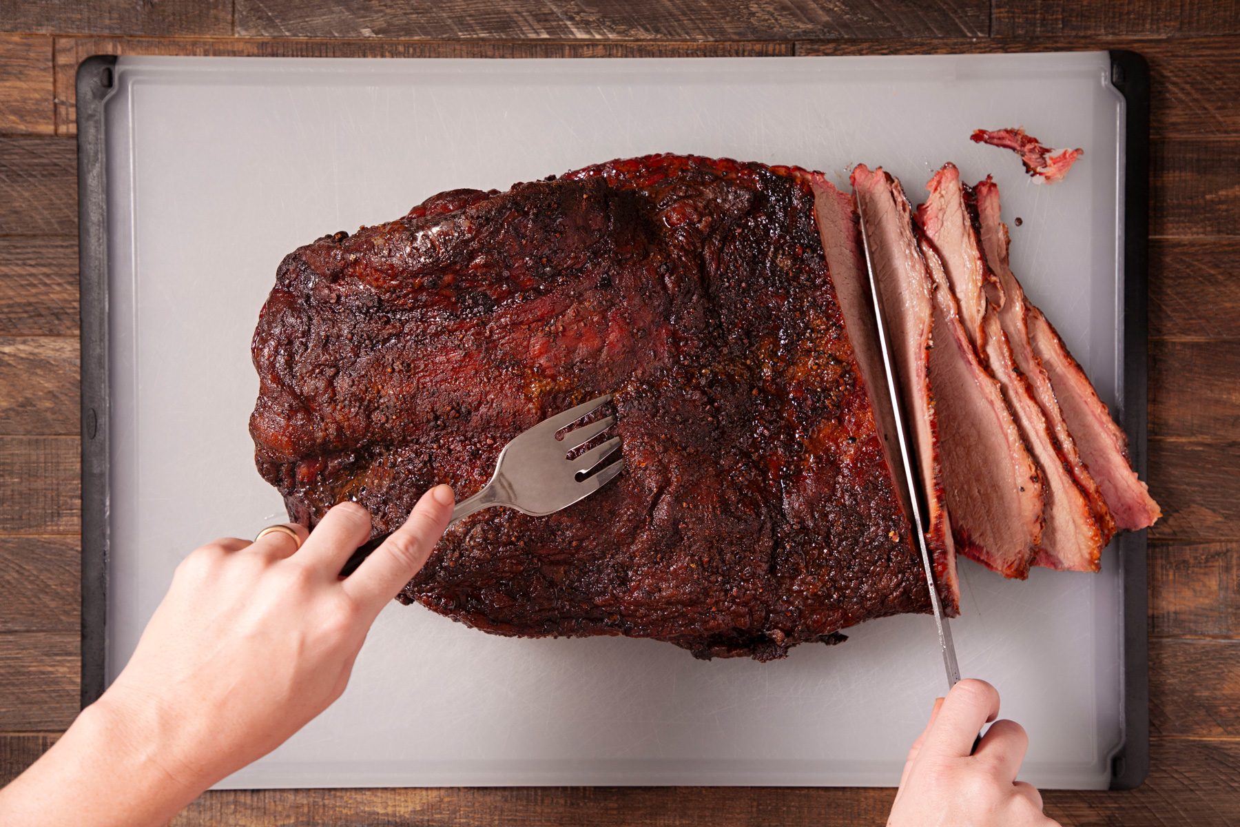 A person is cutting slices of smoked whole brisket.