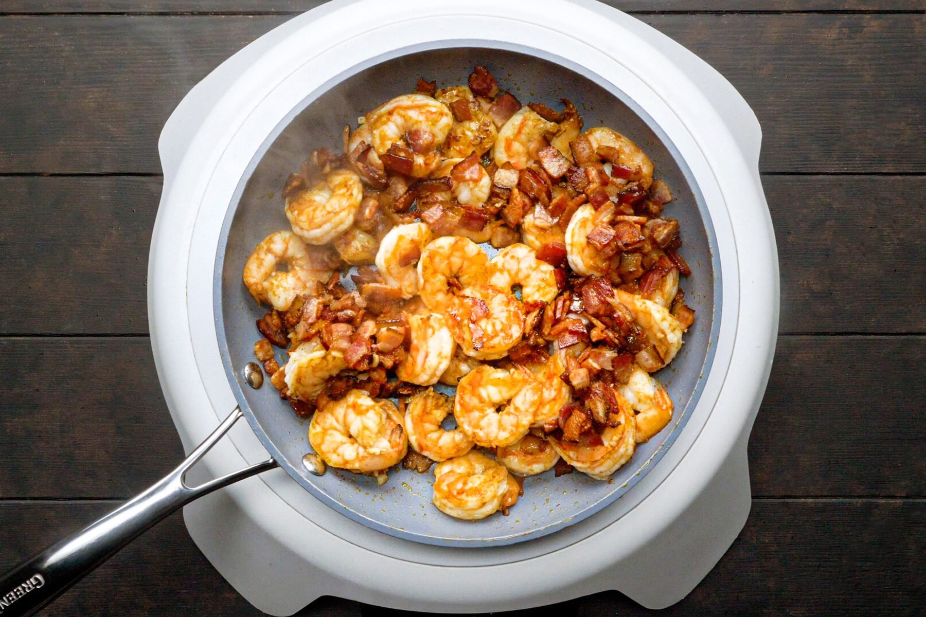 Shrimps and Chopped bacon are cooking in a large skillet