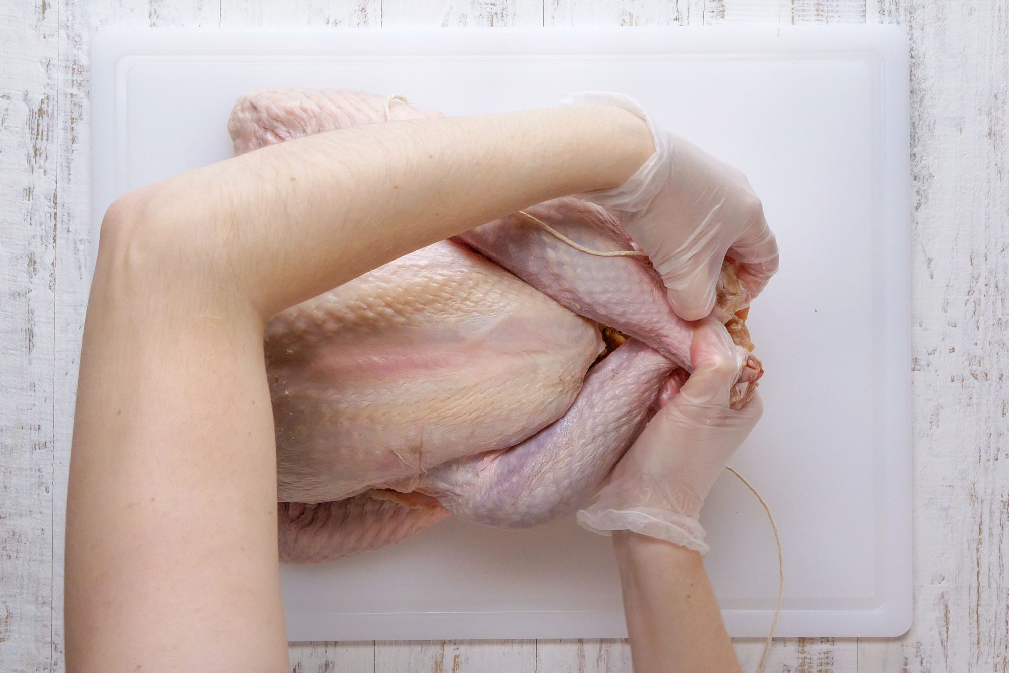 overhead shot of someone tying turkey legs; chopping board; wooden background;