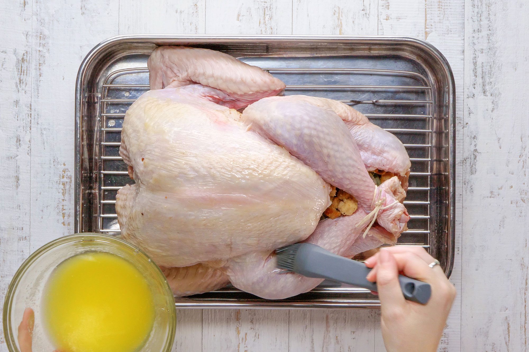 overhead shot of brushing Stuffed Turkey placed in a roasting pan; wooden background;