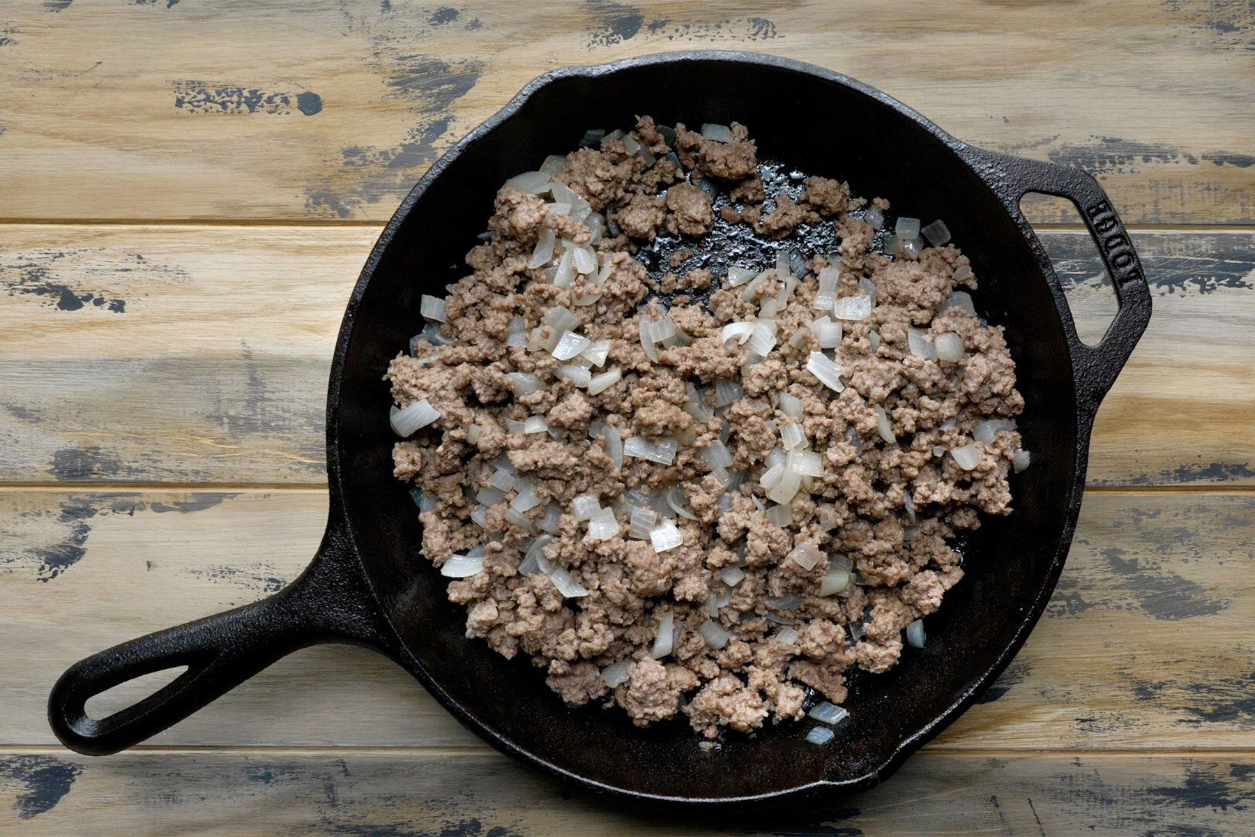 Overhead shot of large skillet; cook beef and onion over medium heat until meat is no longer pink; season with salt and pepper; wooden background;
