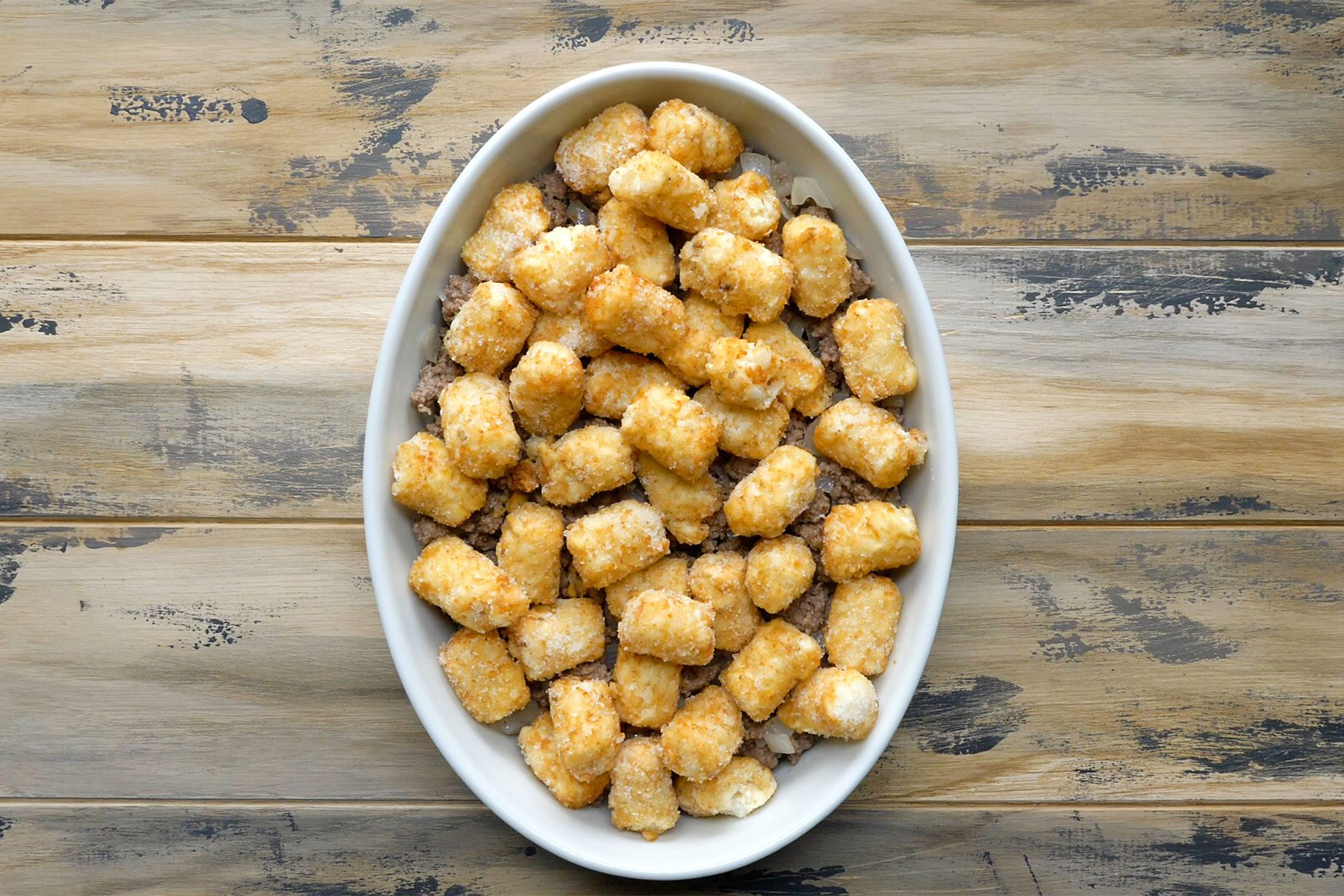 Overhead shot of transfered to a greased baking dish; top with tater tots; wooden background;
