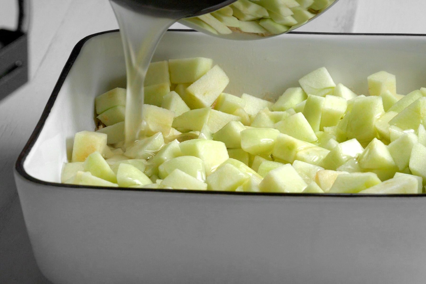 Syrup is pouring over the layer of chopped apples in a baking dish.