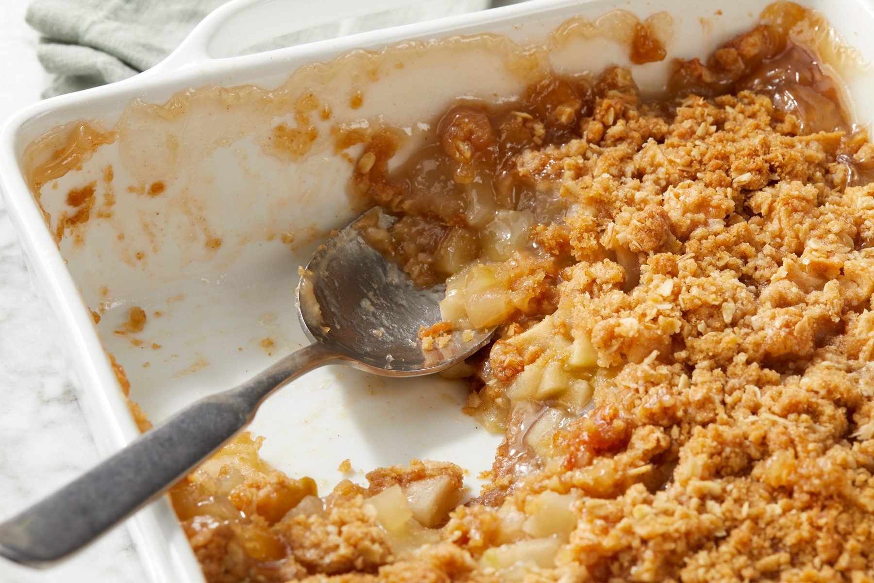 A white baking dish of Winning Apple Crisp with a spoon