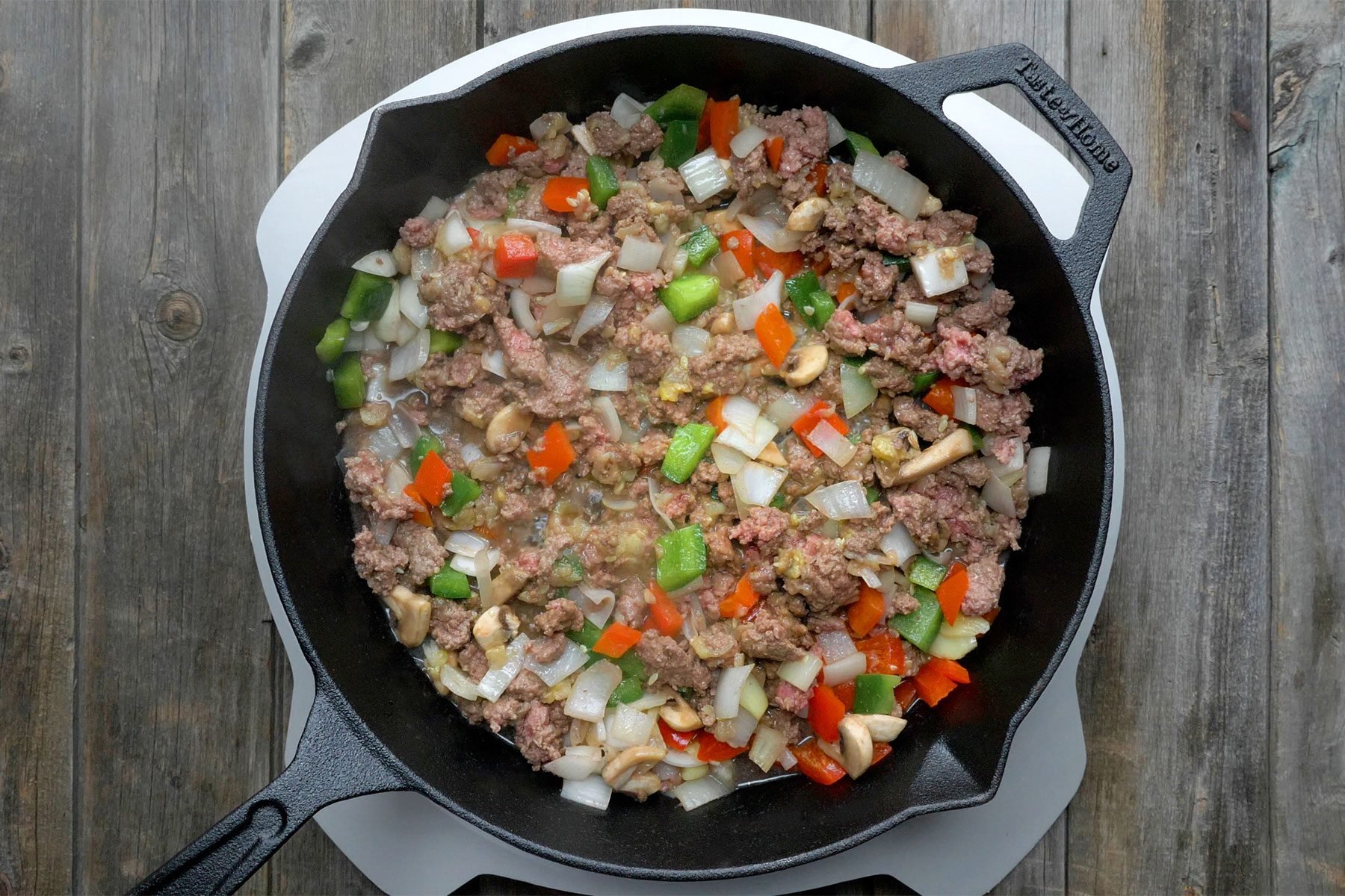 Overhead shot of skillet; cooked beef, zucchini pulp, onion, mushrooms and peppers over medium heat; until meat in no longer pink; induction stove; wooden background;