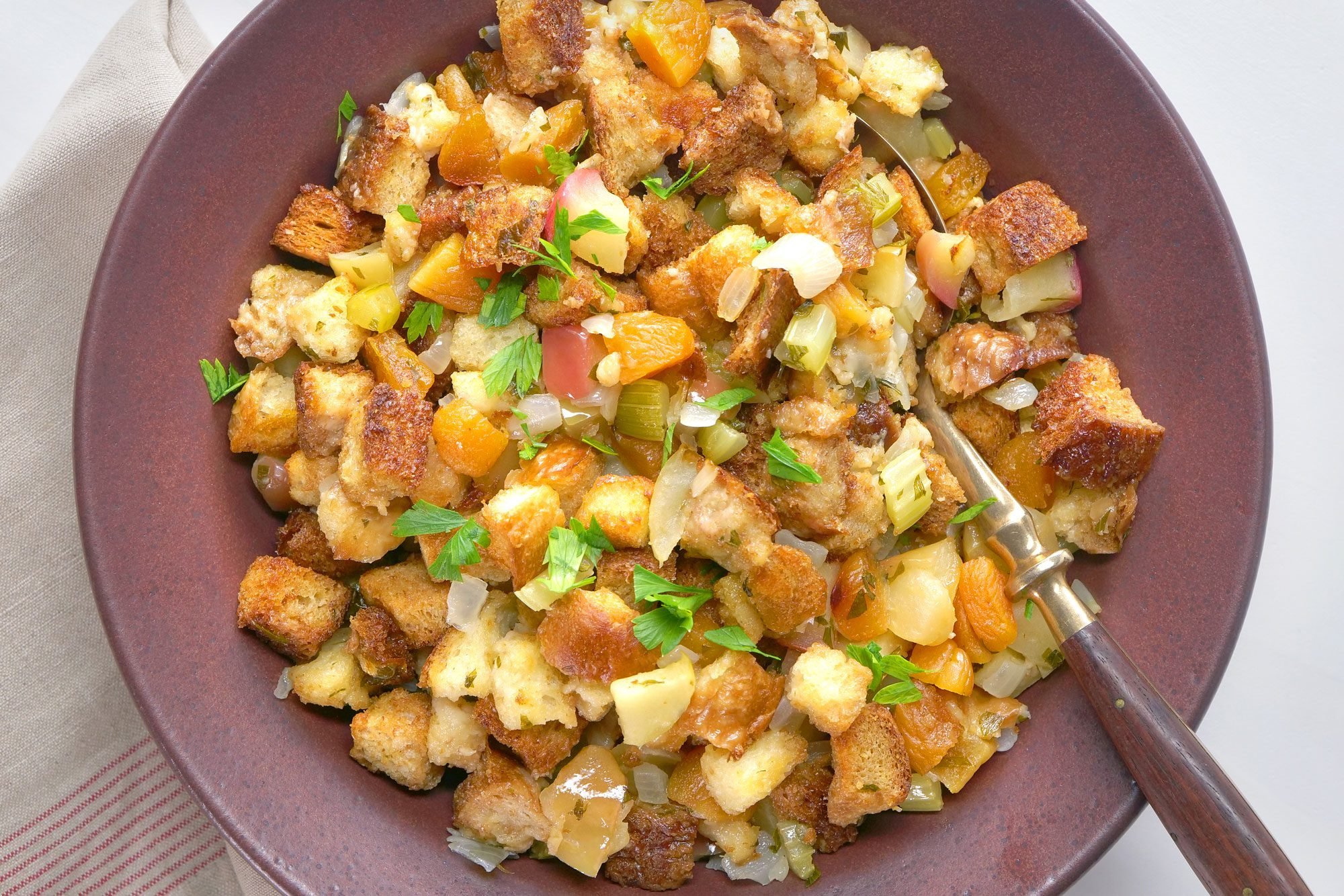 overhead shot; white background; Apple & Apricot Stuffing served in a small plate with spoon over kitchen napkin;