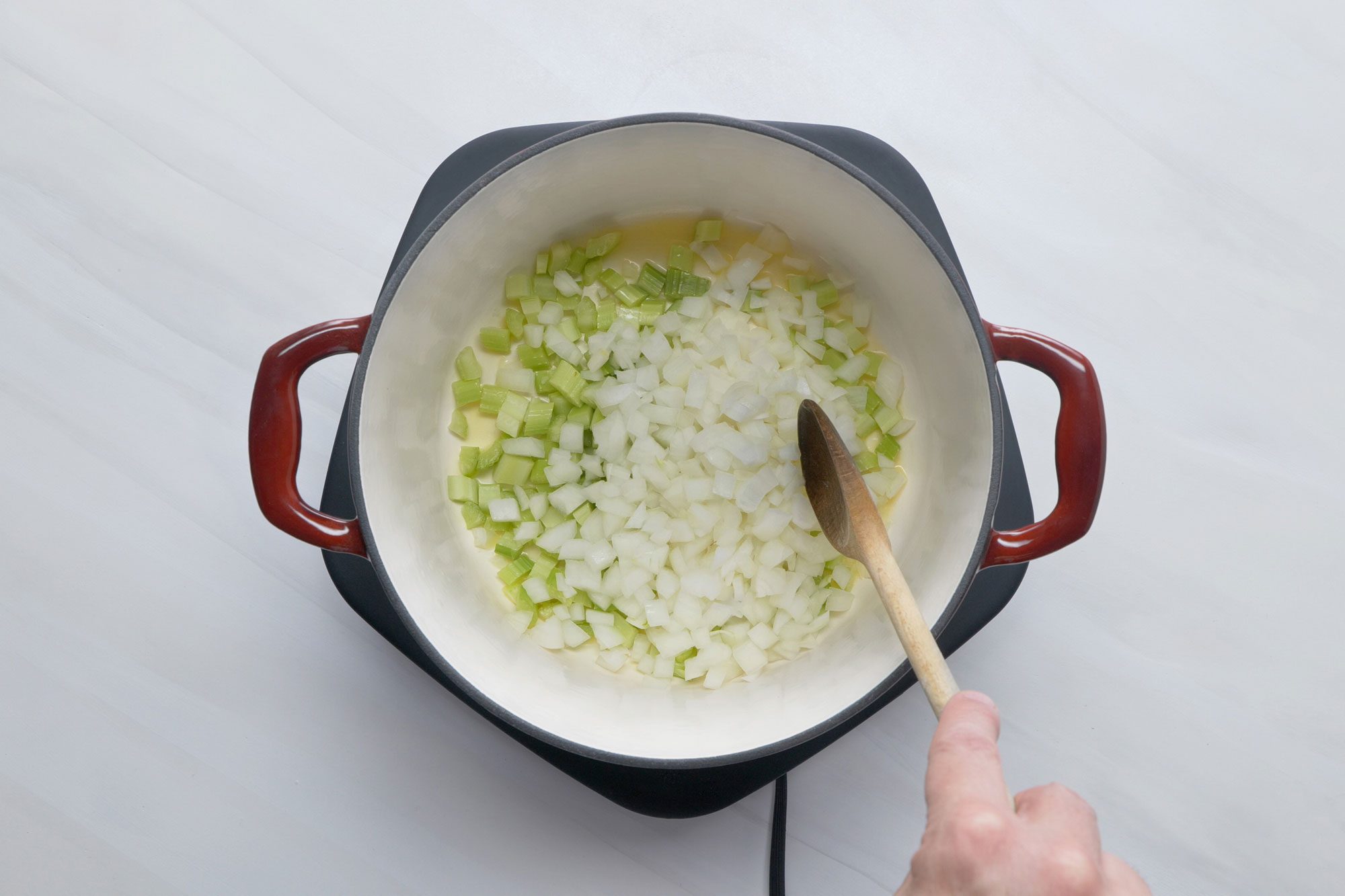 overhead shot; white background; In a Dutch oven, Added celery and onion; cooking and stiring until tender with wooden spatula;